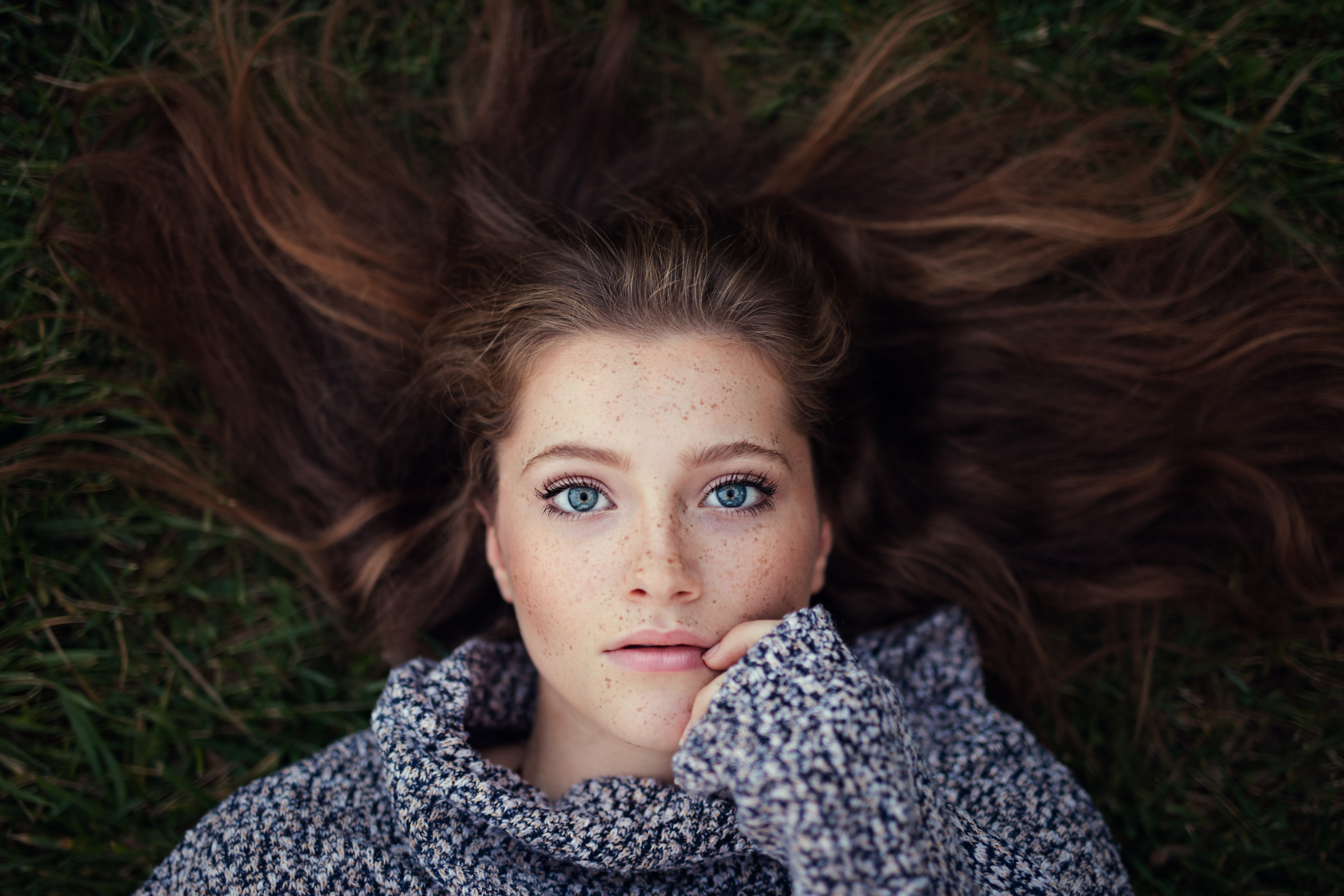 Woman with freckles and blue eyes lying on grass HD Wallpaper