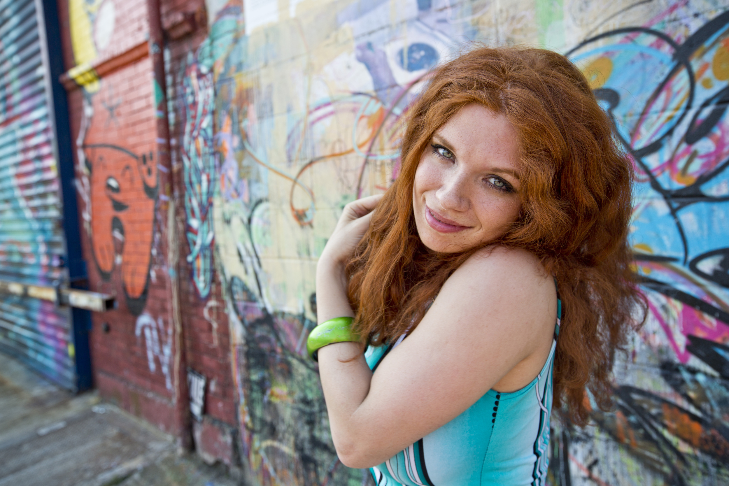 Redhead woman with freckles touching her wavy hair in front of graffiti wall HD Wallpaper