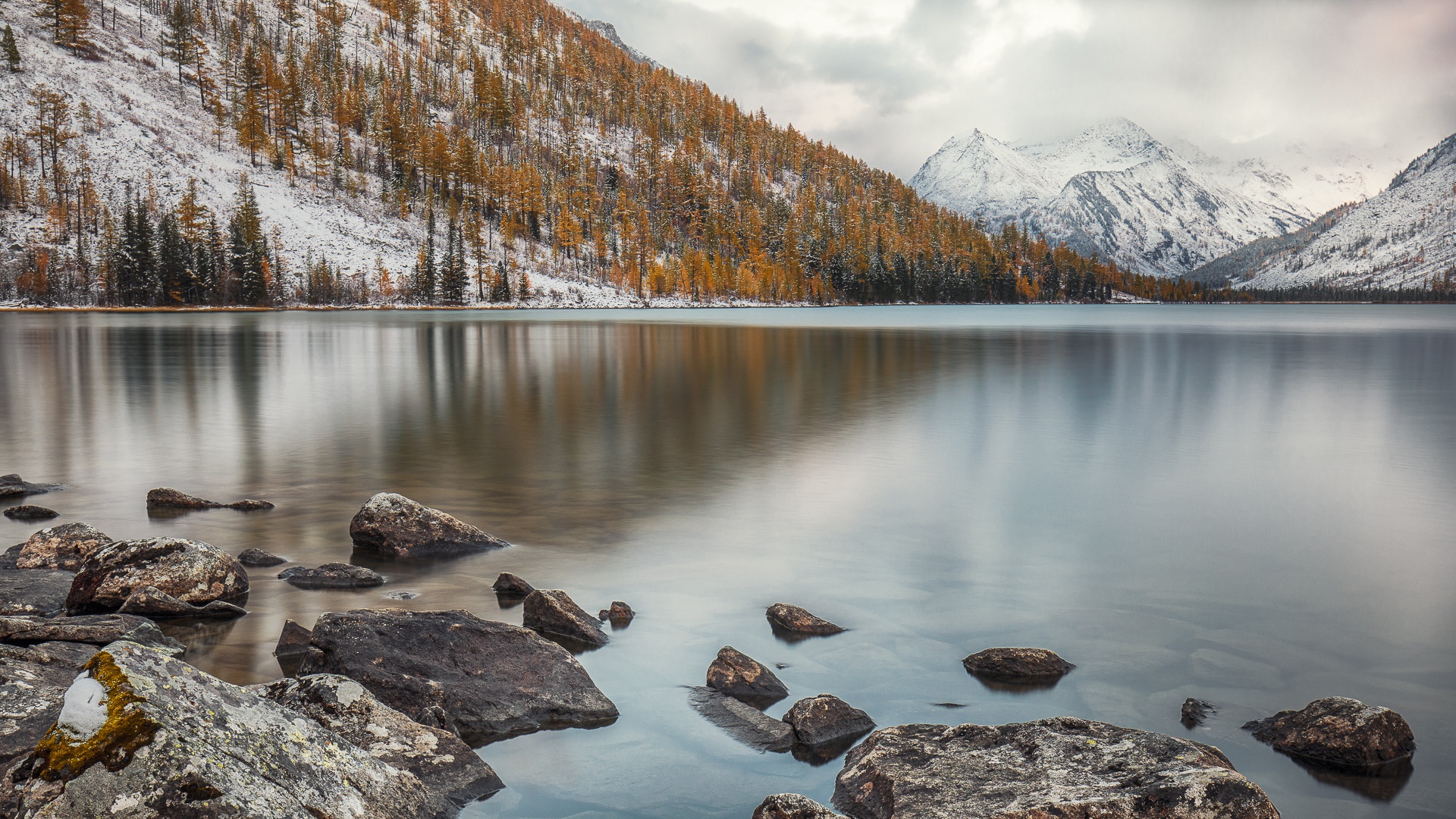Snow-dusted mountains and autumn trees reflected in a calm lake HD Wallpaper