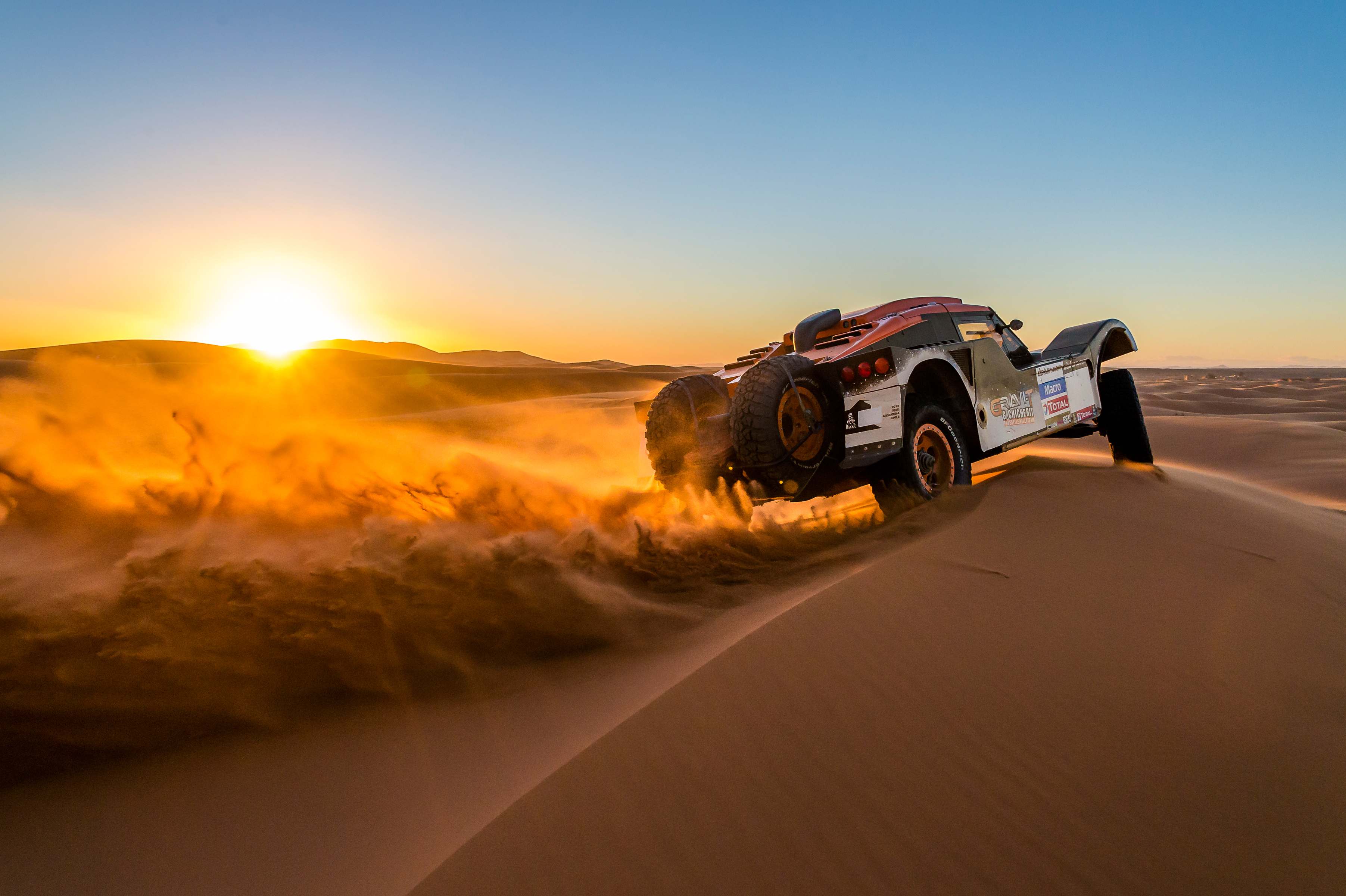 Rally car racing through desert dunes at sunset HD Wallpaper