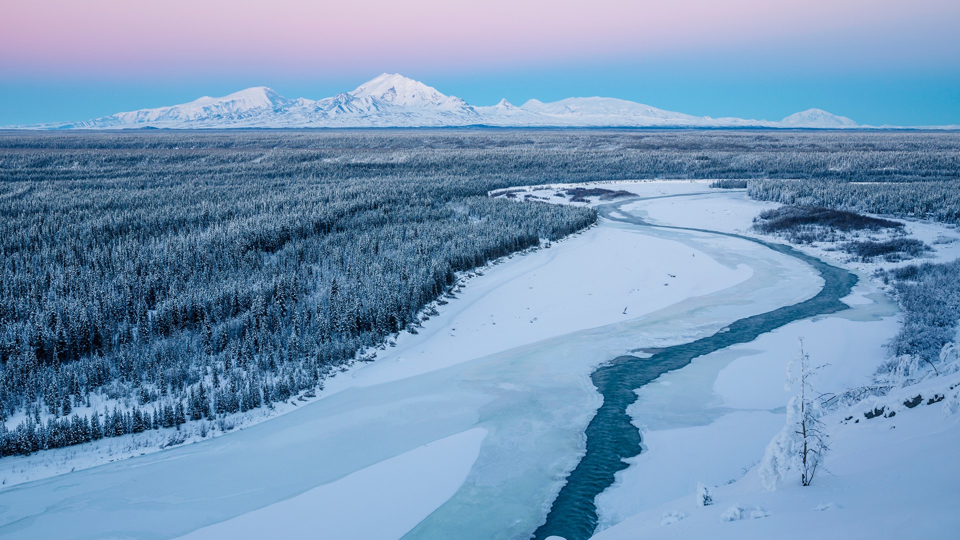Snowy forest and river with mountains in the background HD Wallpaper