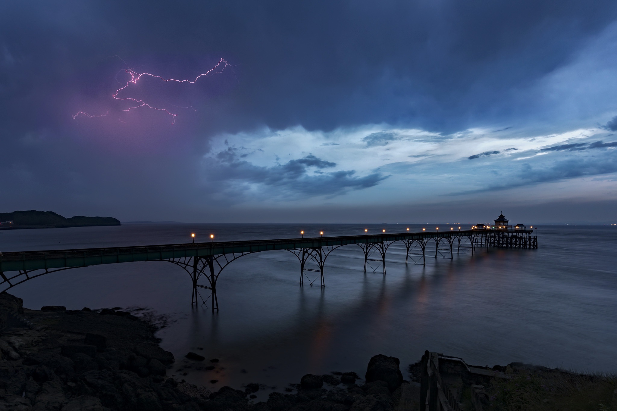 Pier during a lightning storm over the sea HD Wallpaper