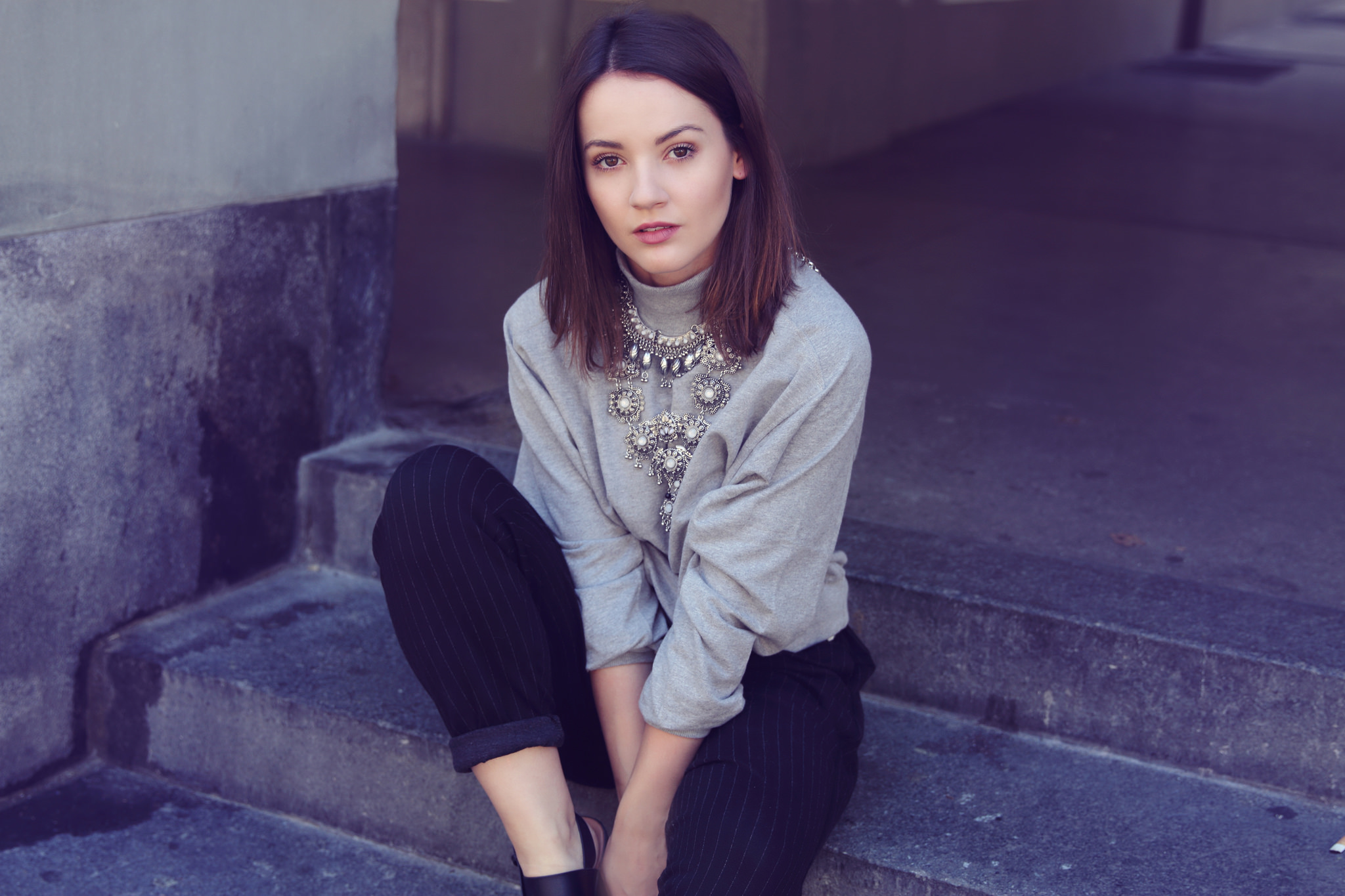 Woman wearing a grey shirt and necklace sitting on steps HD Wallpaper