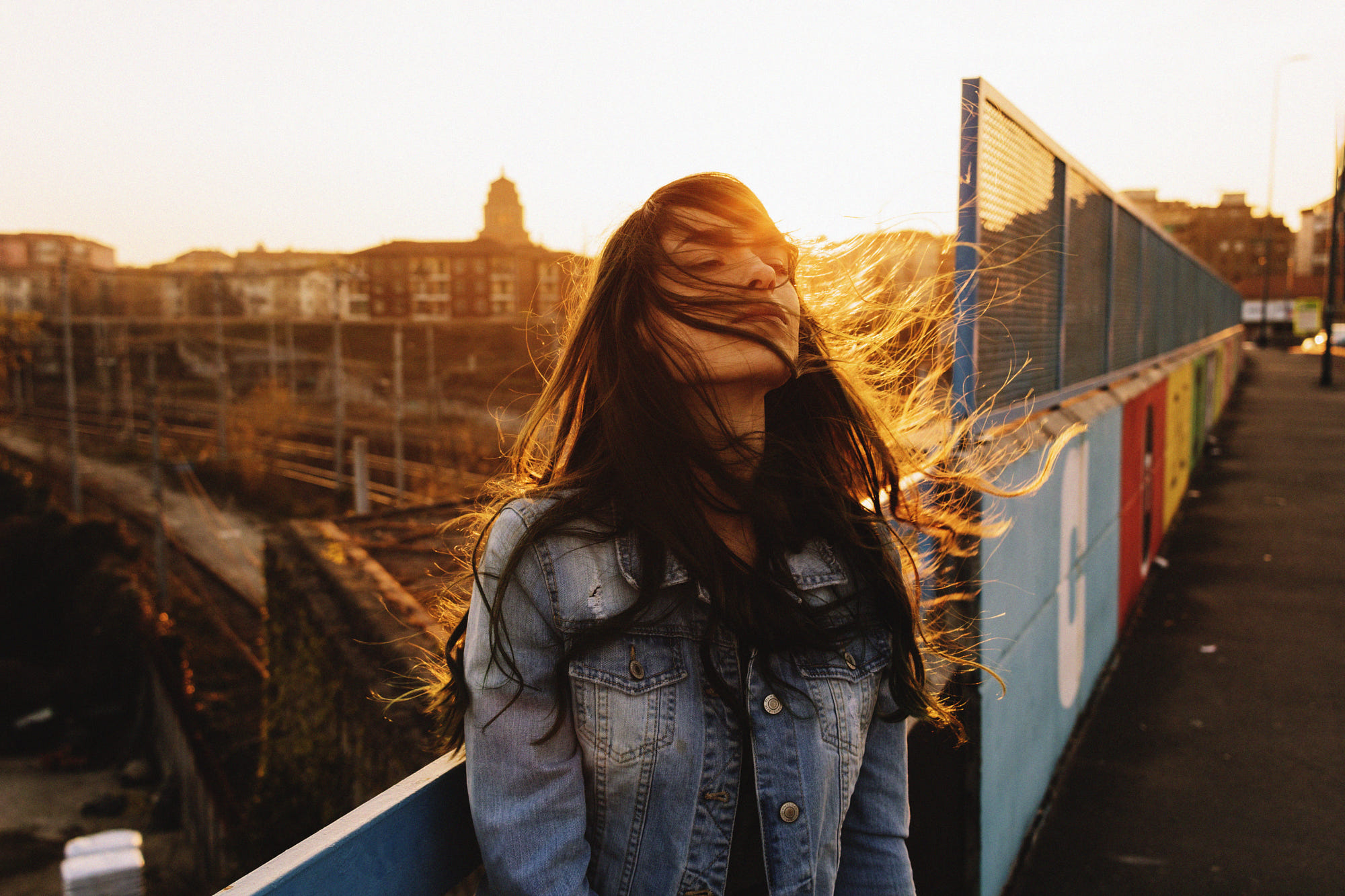 Woman in denim jacket with hair blowing in the wind at sunset HD Wallpaper