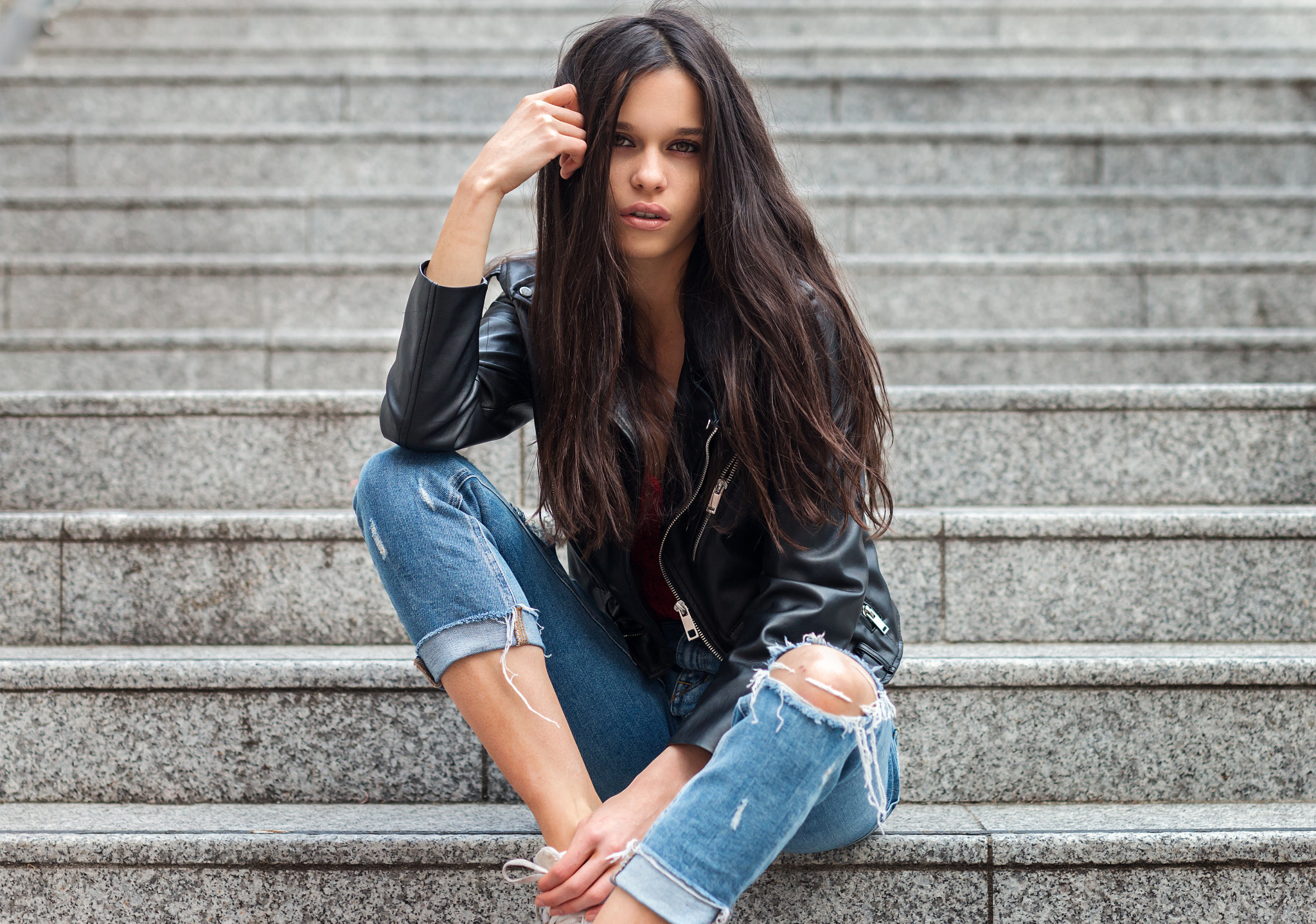 Woman in leather jacket and torn jeans sitting on stairs HD Wallpaper