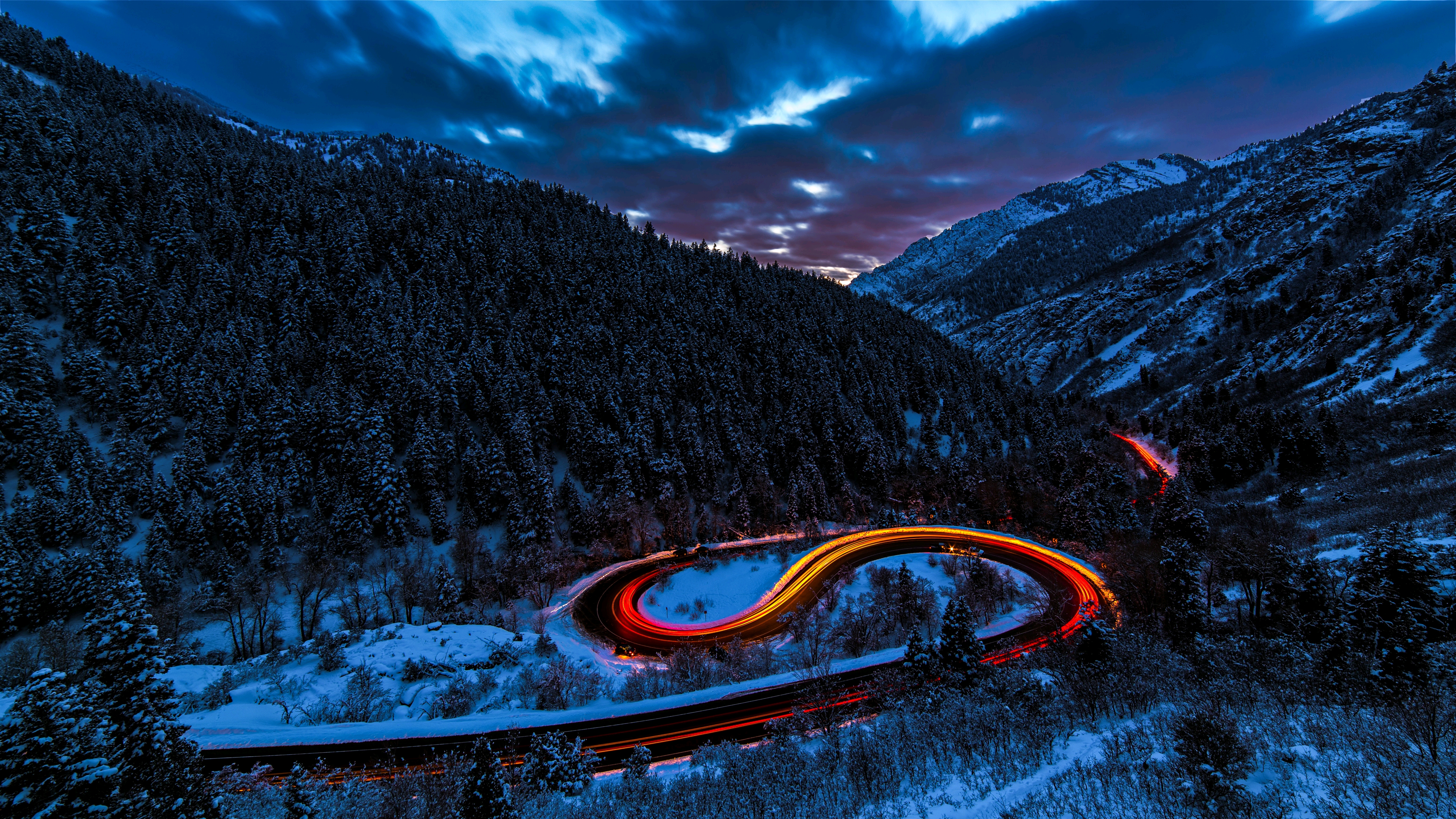 Long exposure of a winding road through a snowy mountain forest at dusk HD Wallpaper