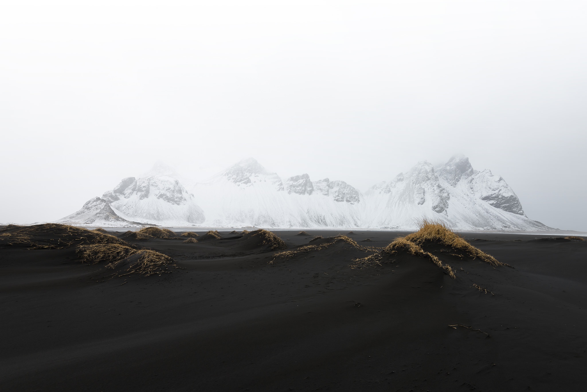 Snow-capped mountains over black sand dunes HD Wallpaper