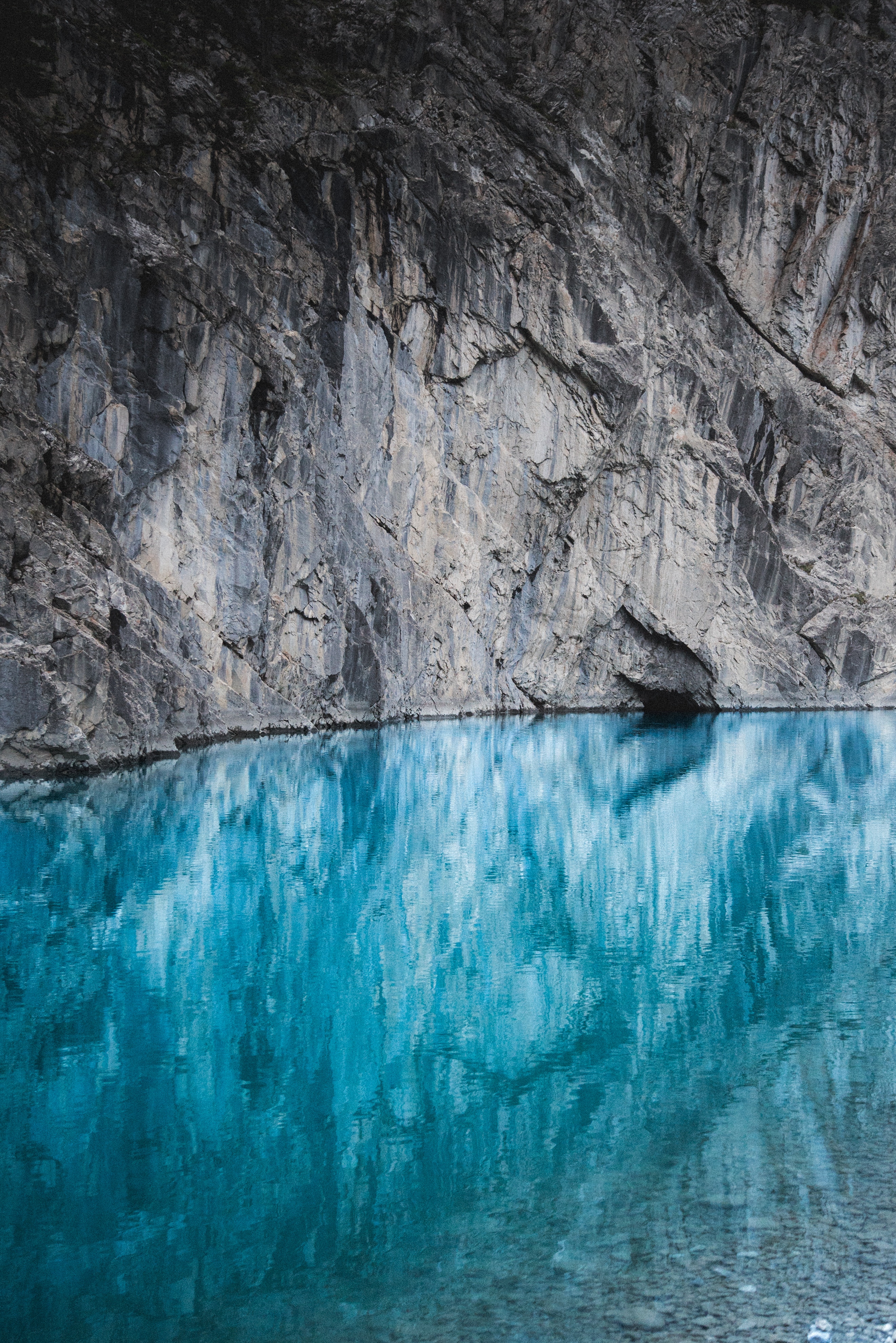 Turquoise lake reflecting a rocky cliff face HD Wallpaper