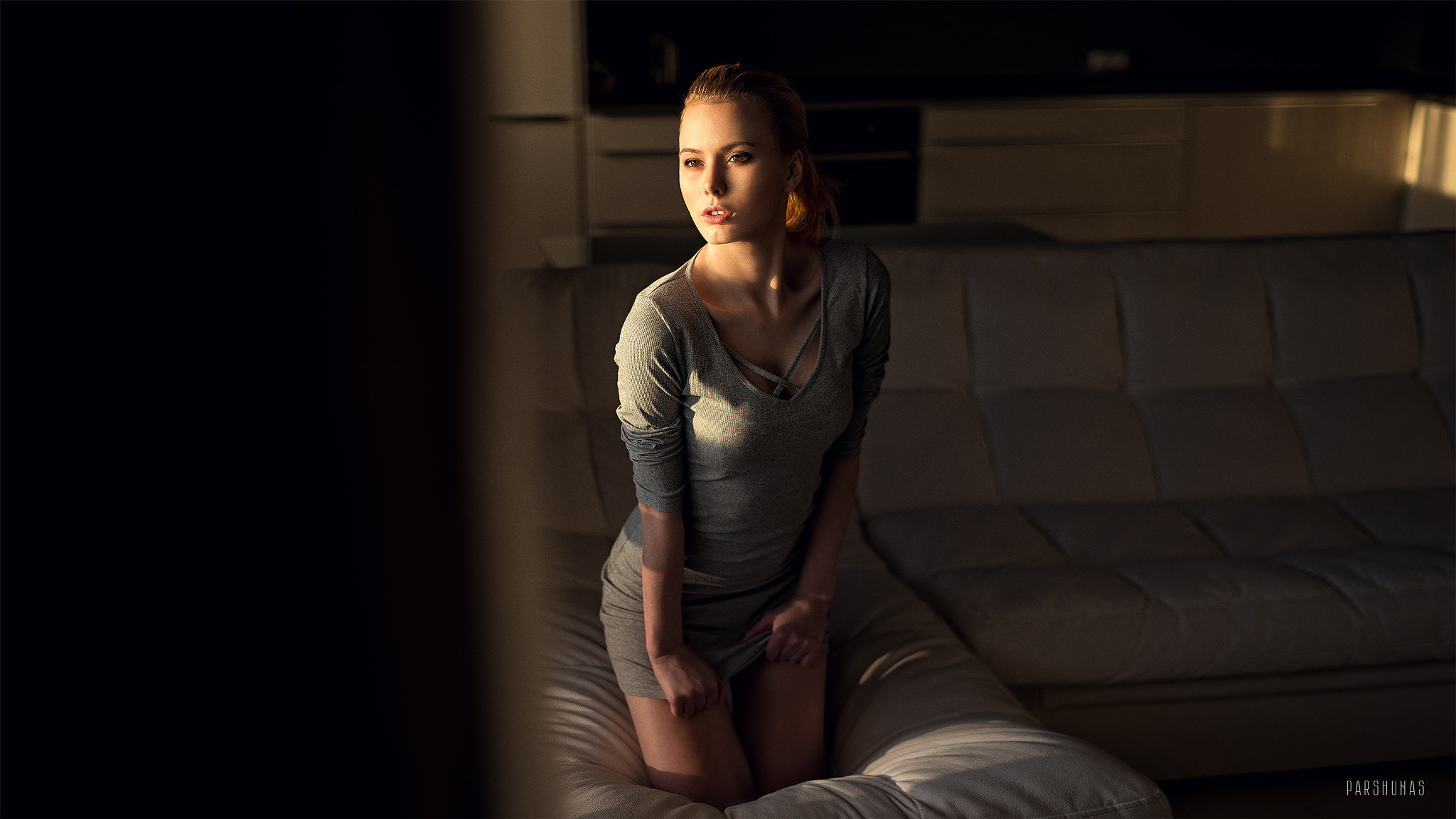 Woman in grey dress kneeling on a couch HD Wallpaper