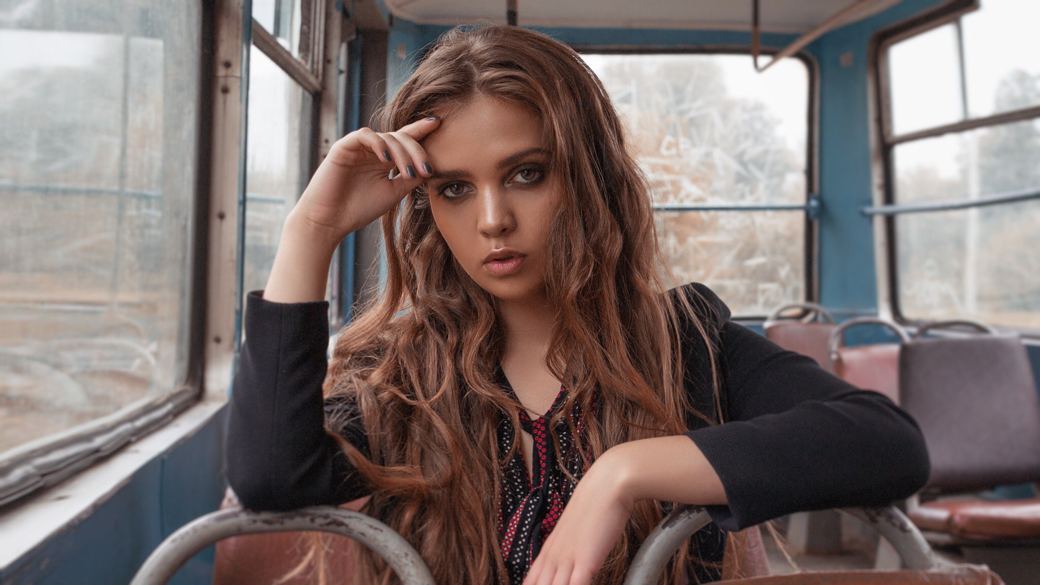 Woman with long wavy hair in a black coat inside a tram HD Wallpaper