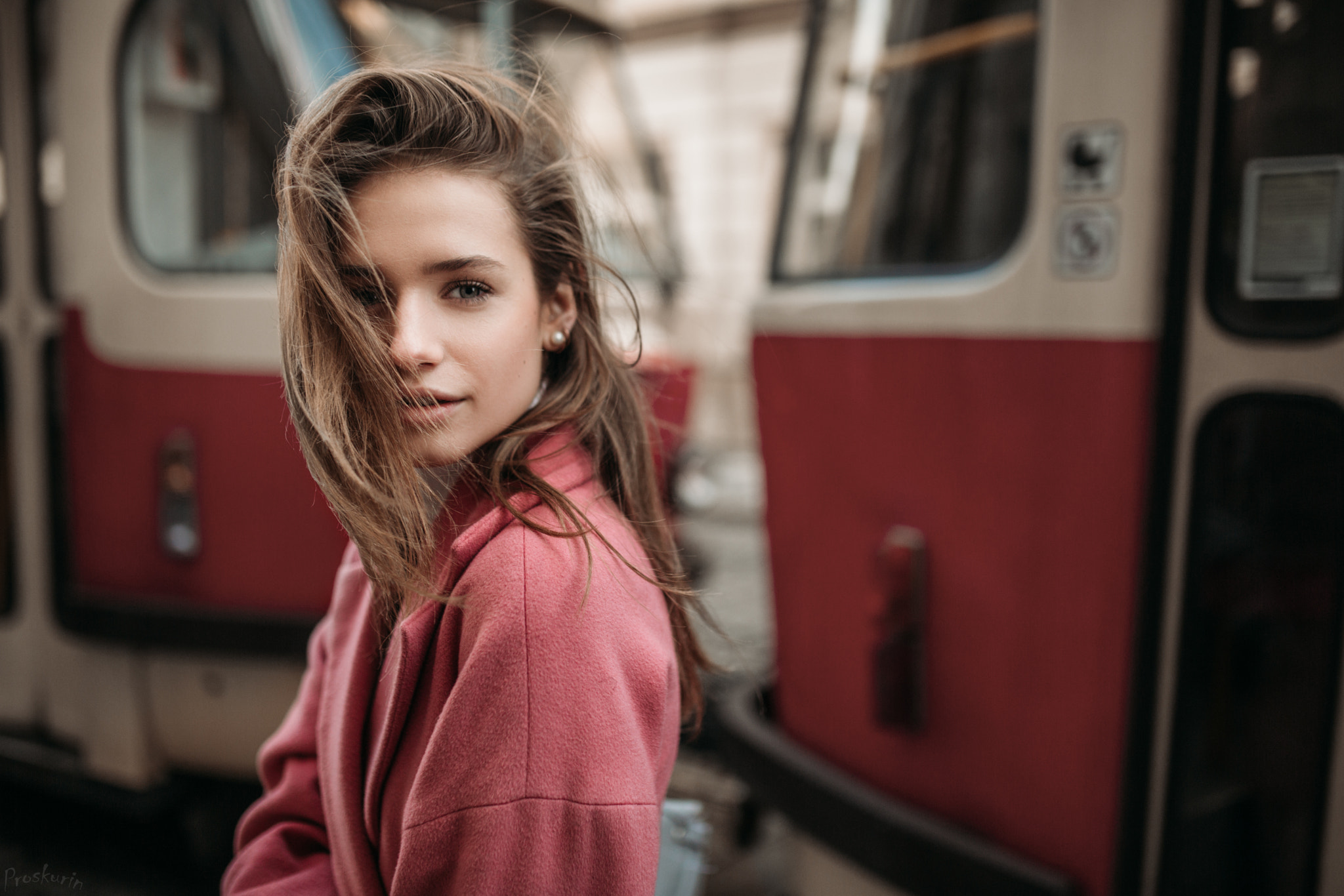 Woman with hair in face, wearing pink coat, with tram in background HD Wallpaper