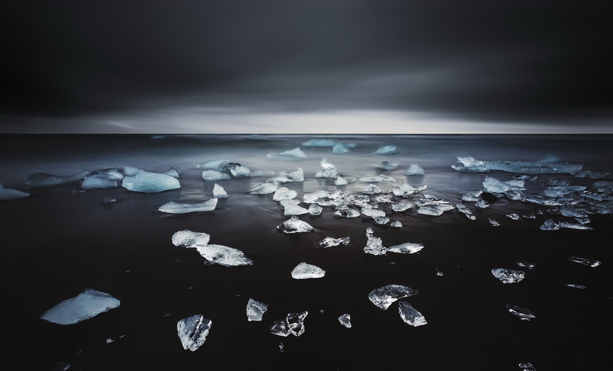 Ice chunks on a dark beach with a stormy sea and sky HD Wallpaper