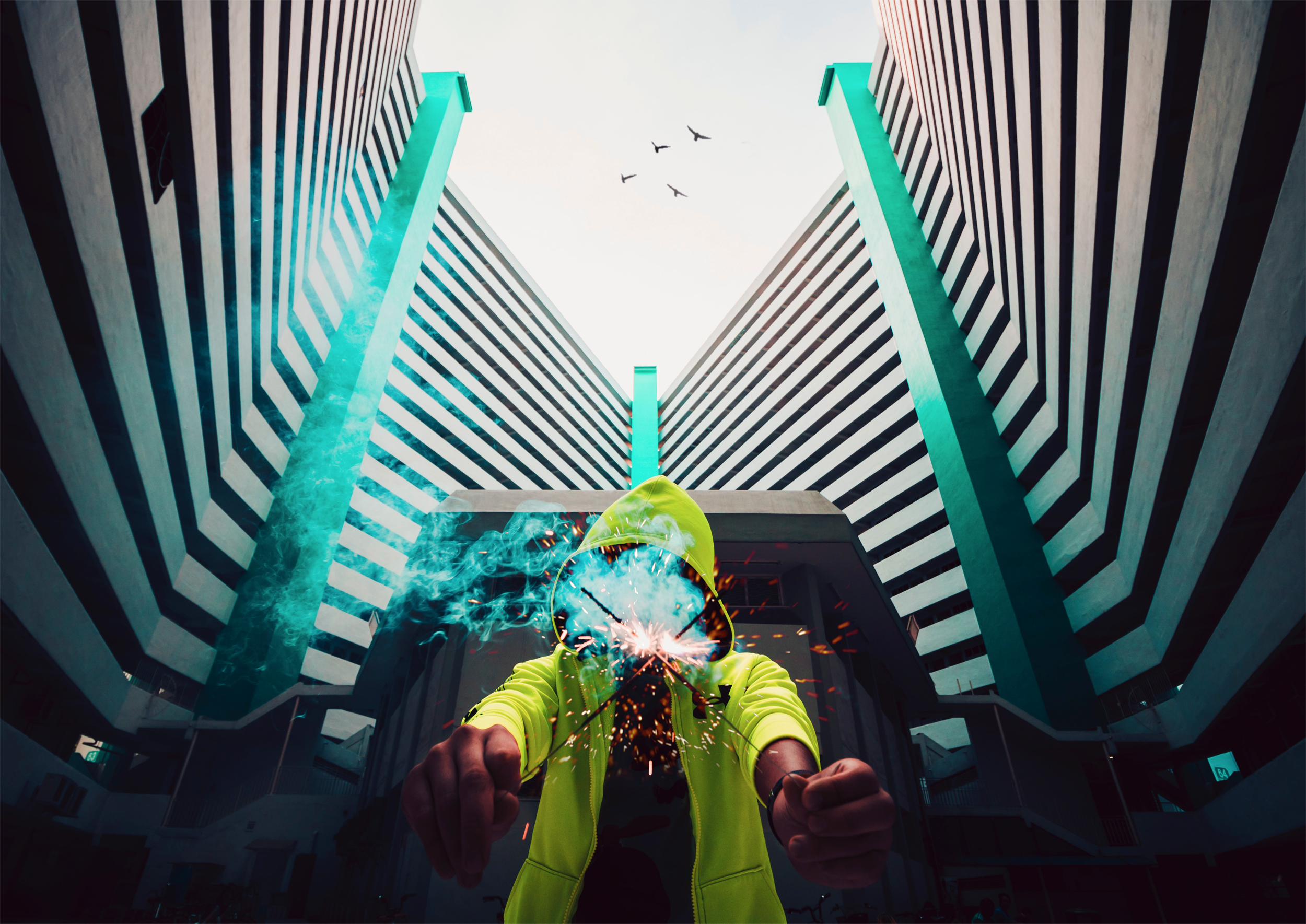 Person in hoodie with sparks in front of modern buildings HD Wallpaper
