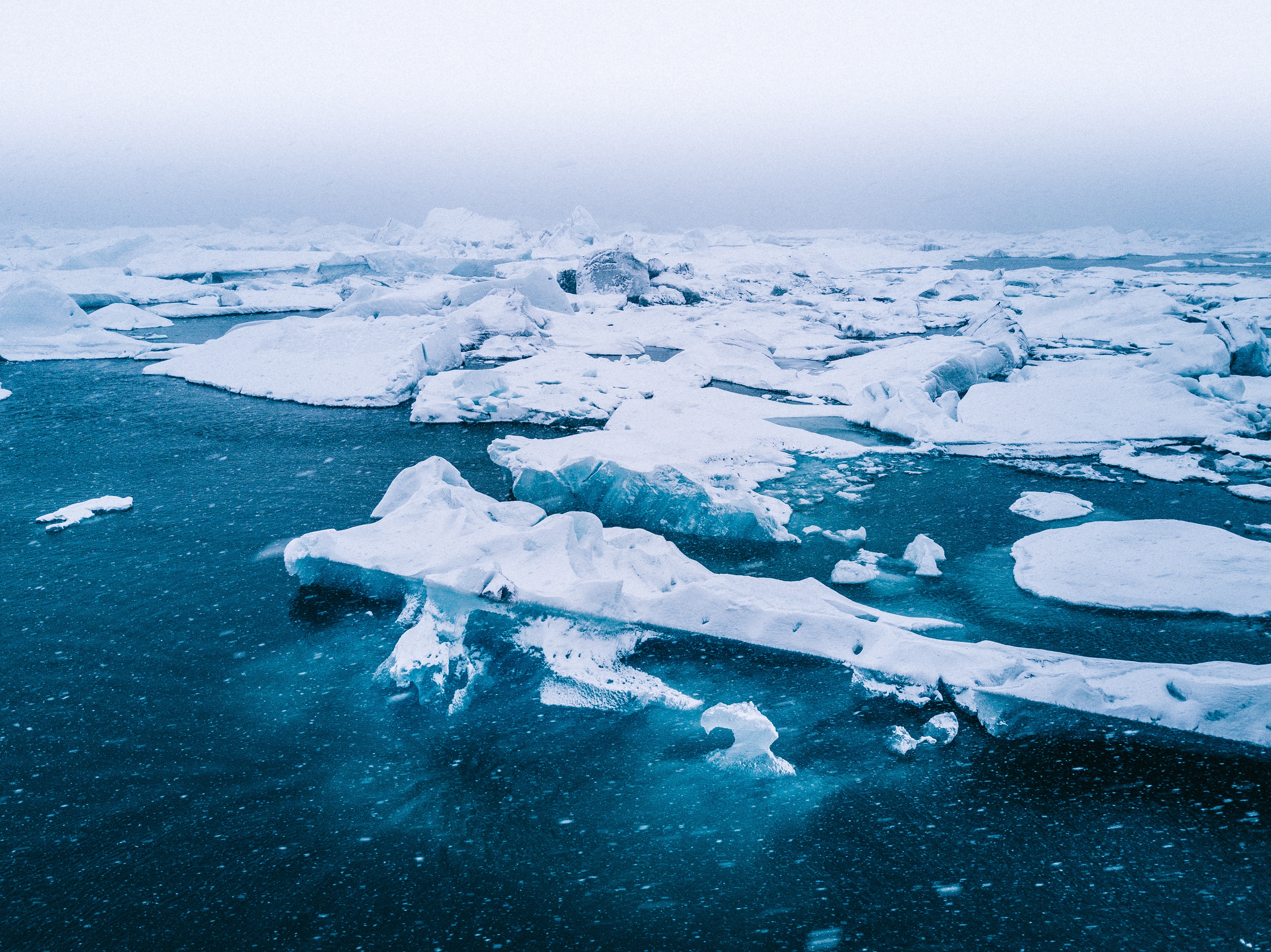 Icebergs floating in dark blue water under a hazy sky HD Wallpaper