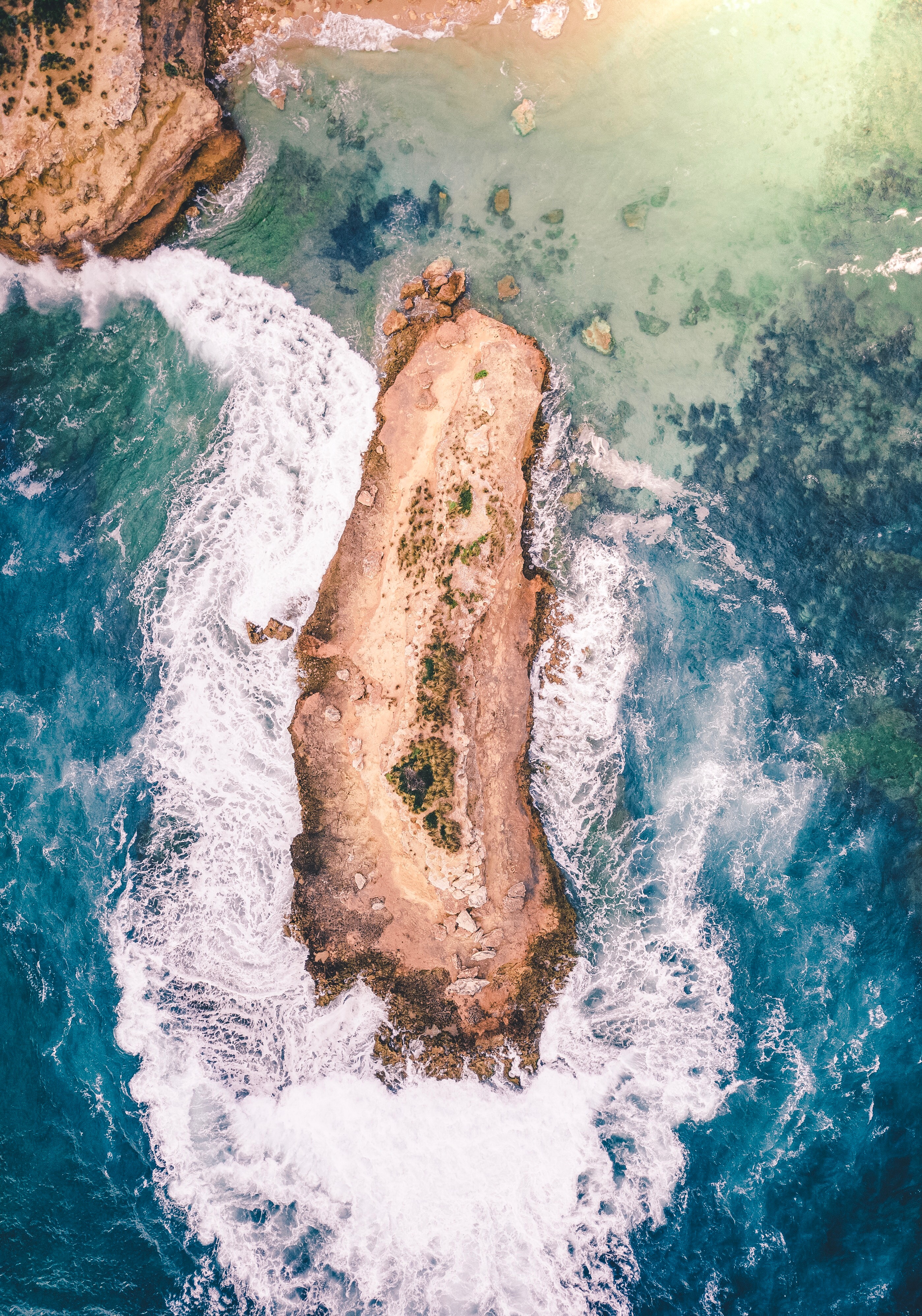 Aerial view of a rocky island surrounded by ocean waves HD Wallpaper