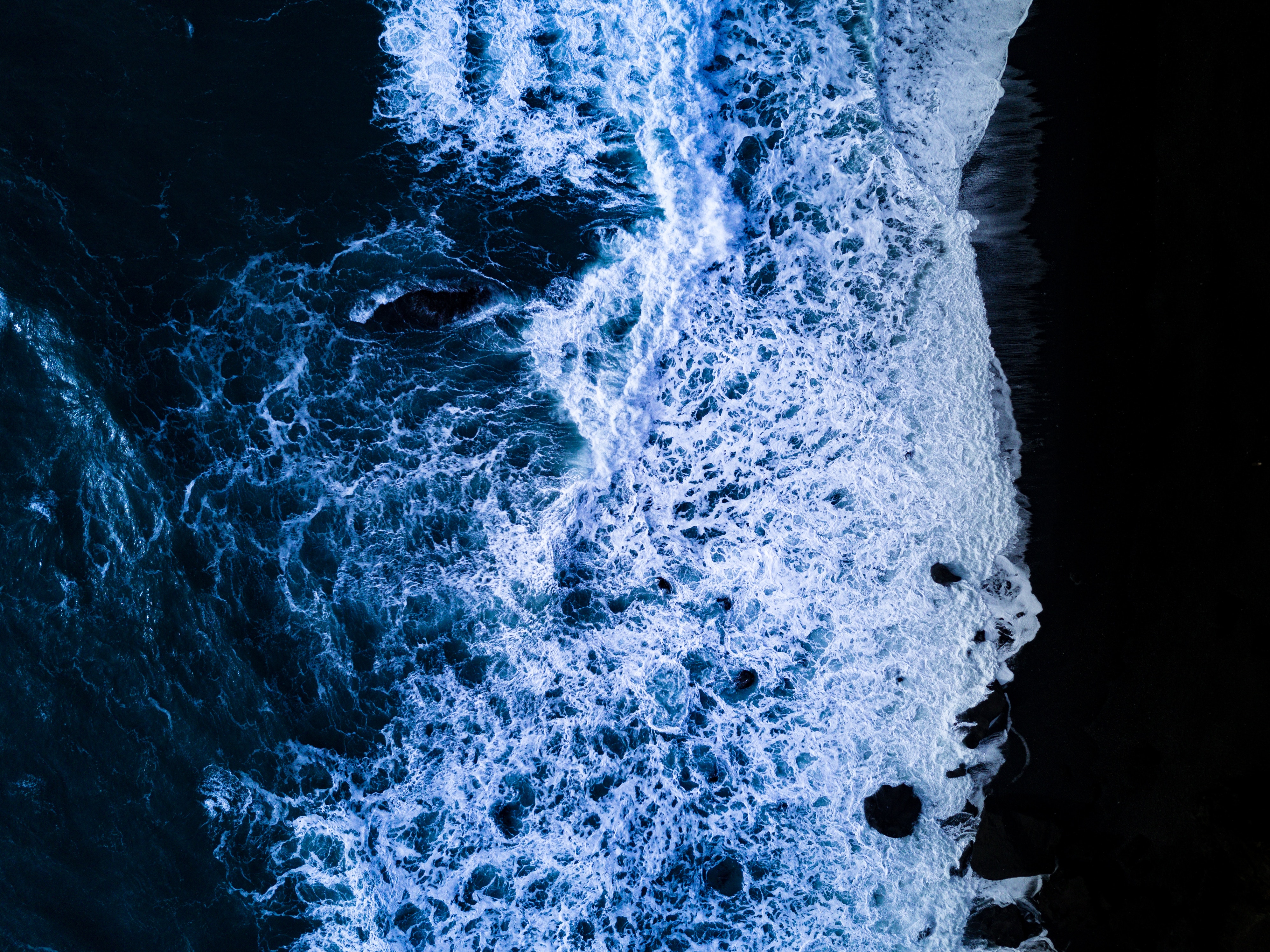 Aerial view of ocean waves crashing on a dark shore HD Wallpaper