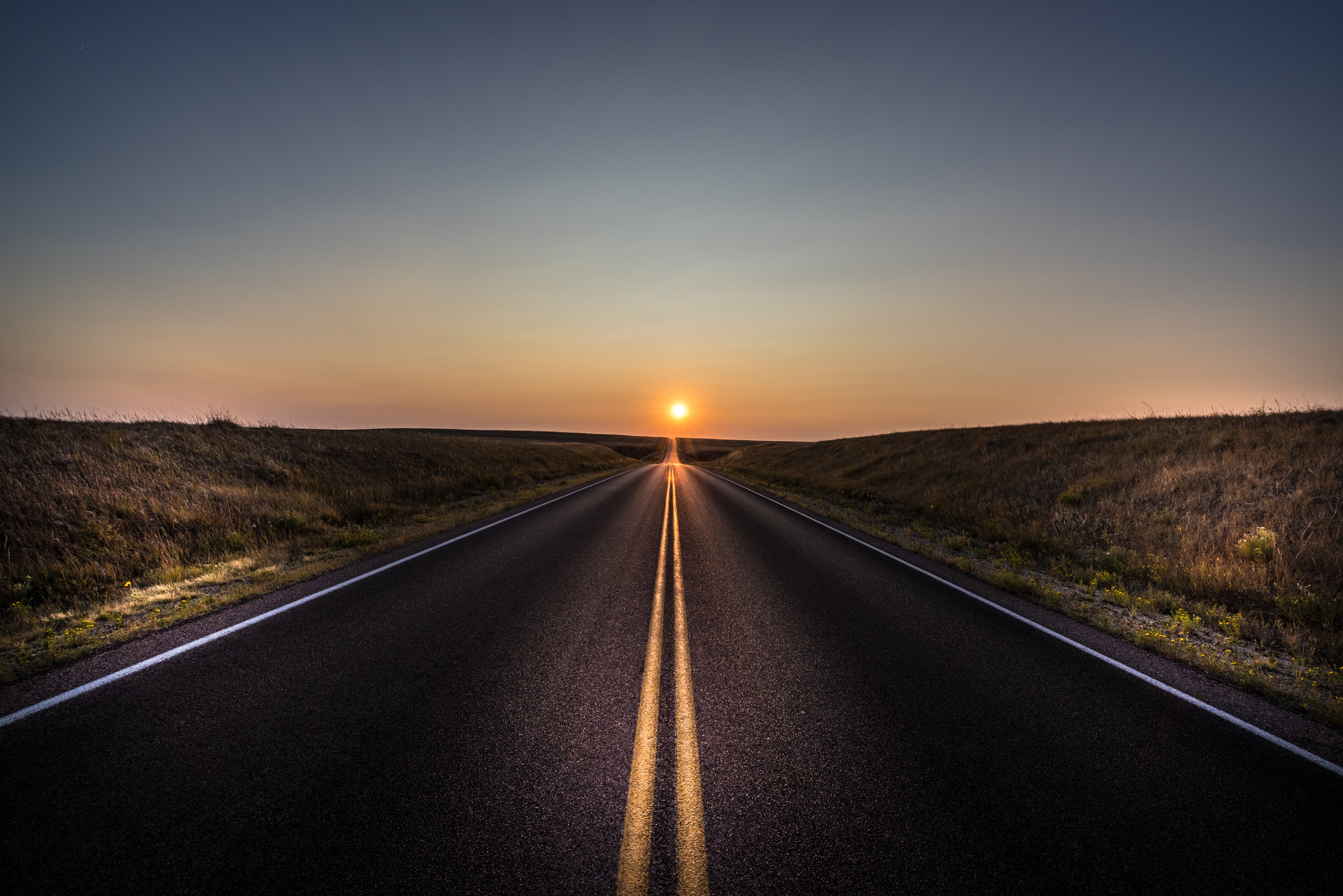 Asphalt road leading to the sunset over a prairie landscape HD Wallpaper
