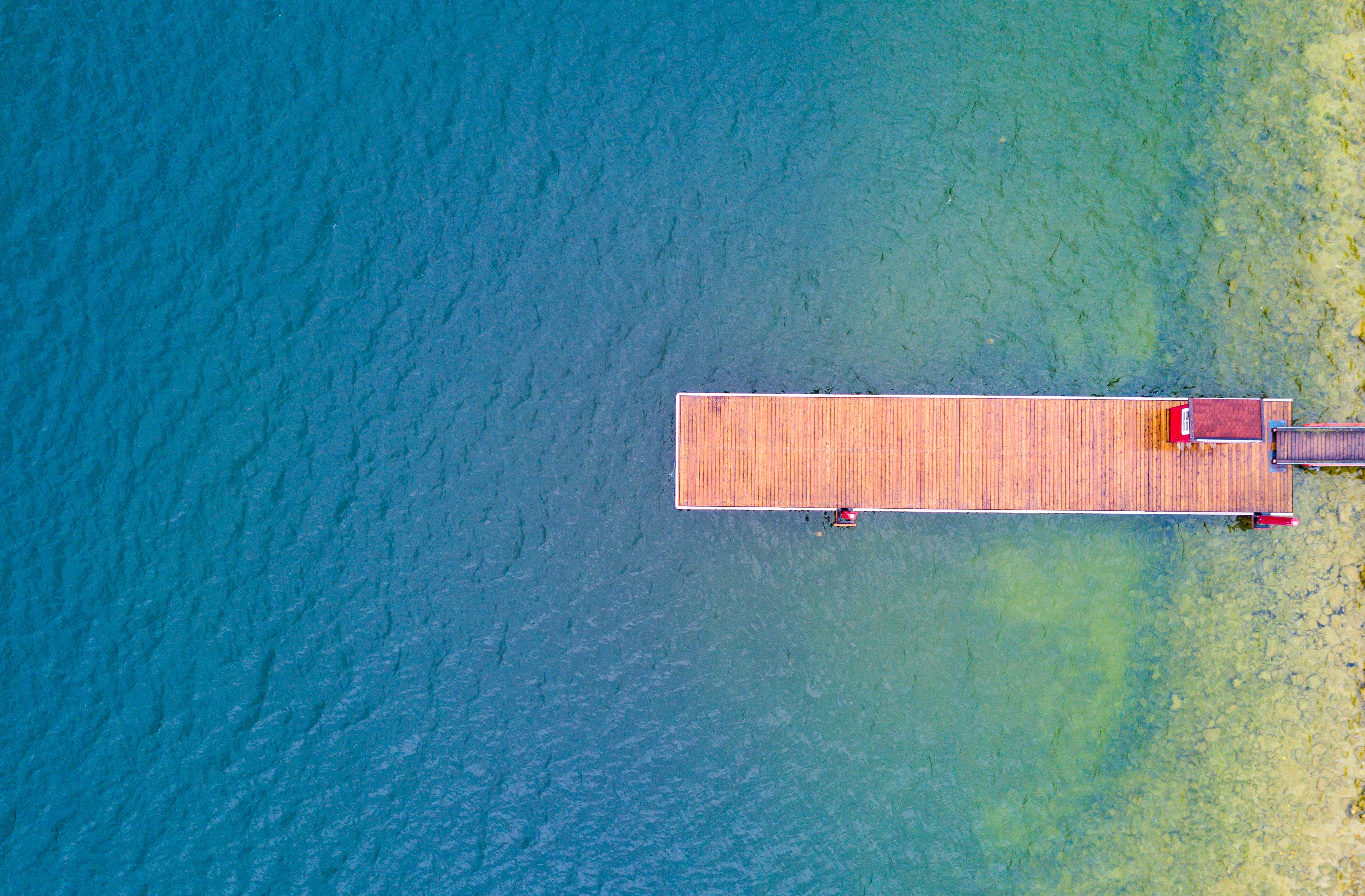 Aerial view of a wooden pier on a blue lake HD Wallpaper