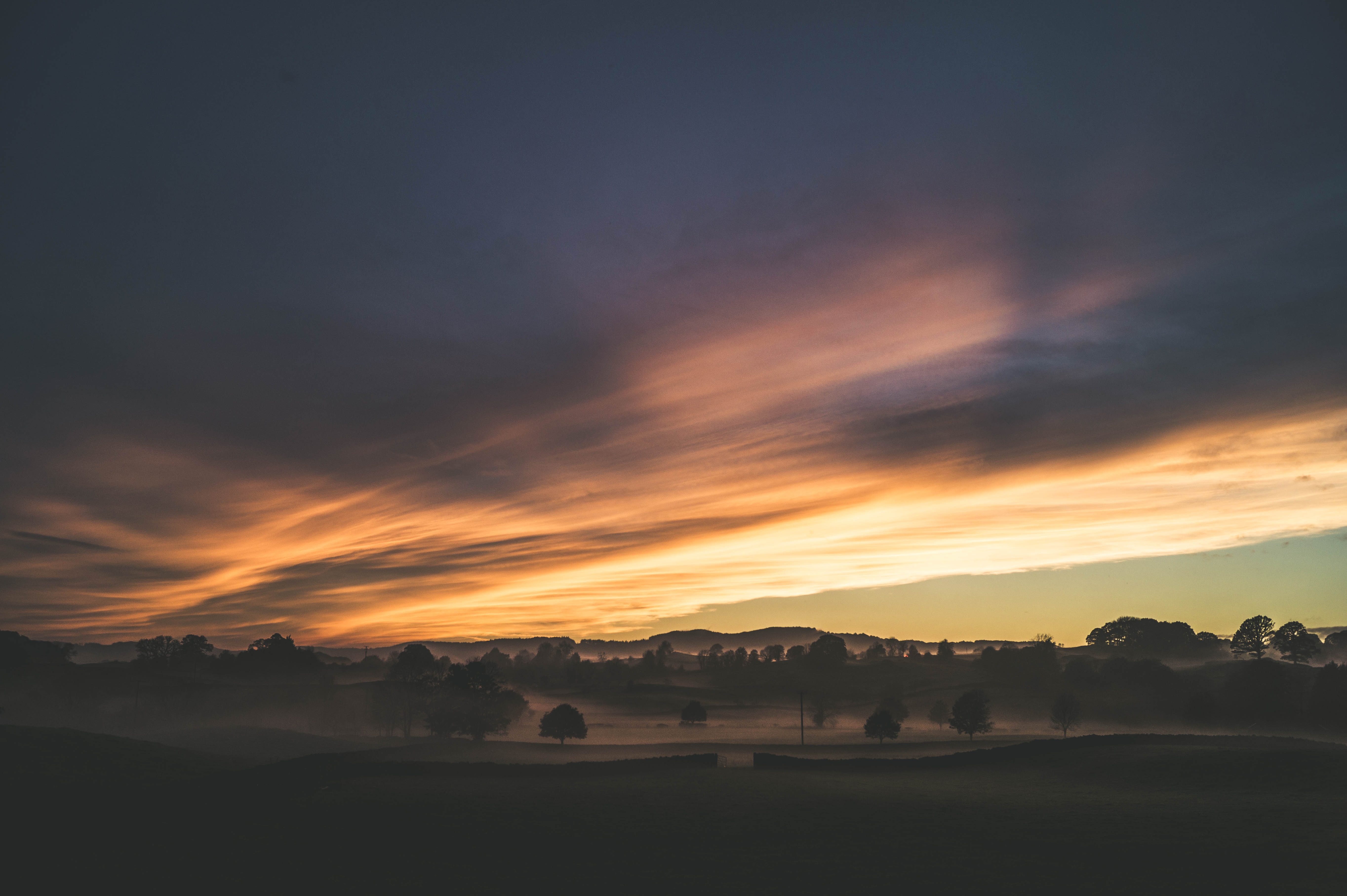 Misty landscape with dramatic sunset clouds over UK countryside HD Wallpaper