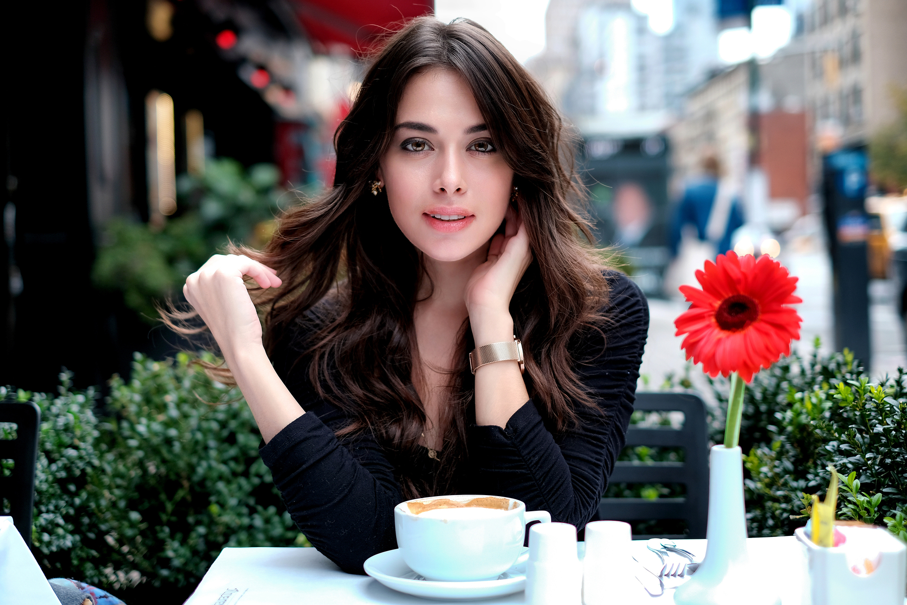 Woman with long brown hair at an outdoor cafe with coffee and a red flower HD Wallpaper