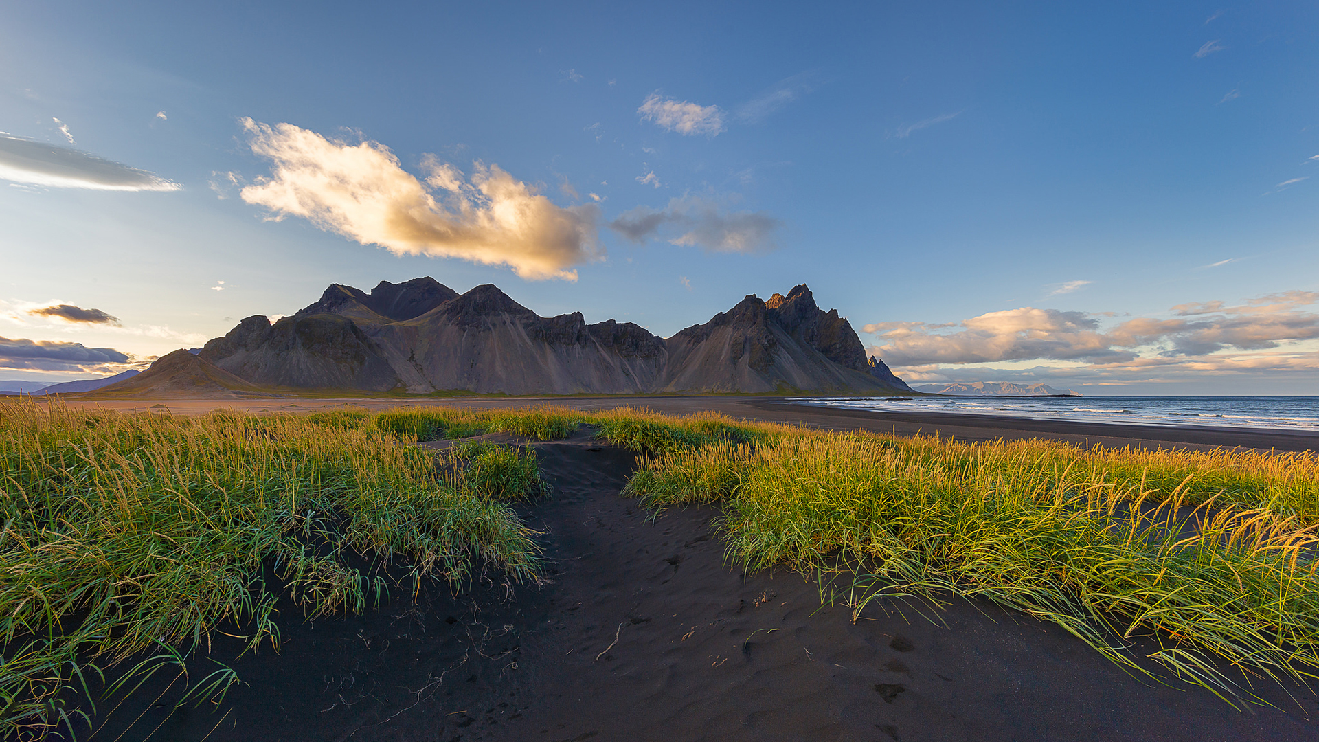 Black sand beach with grass and mountains HD Wallpaper