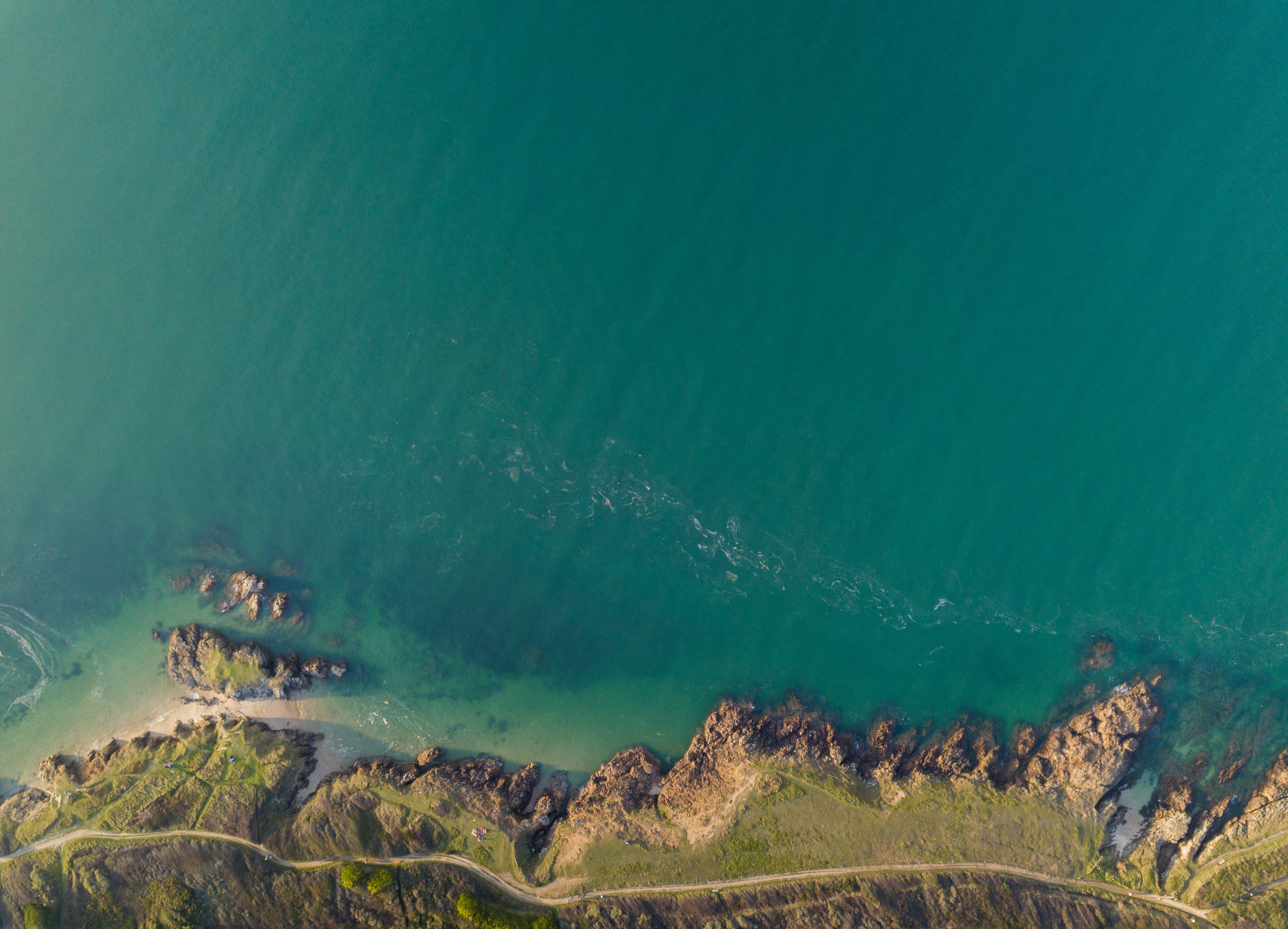 Aerial view of a rocky coastline meeting turquoise water HD Wallpaper