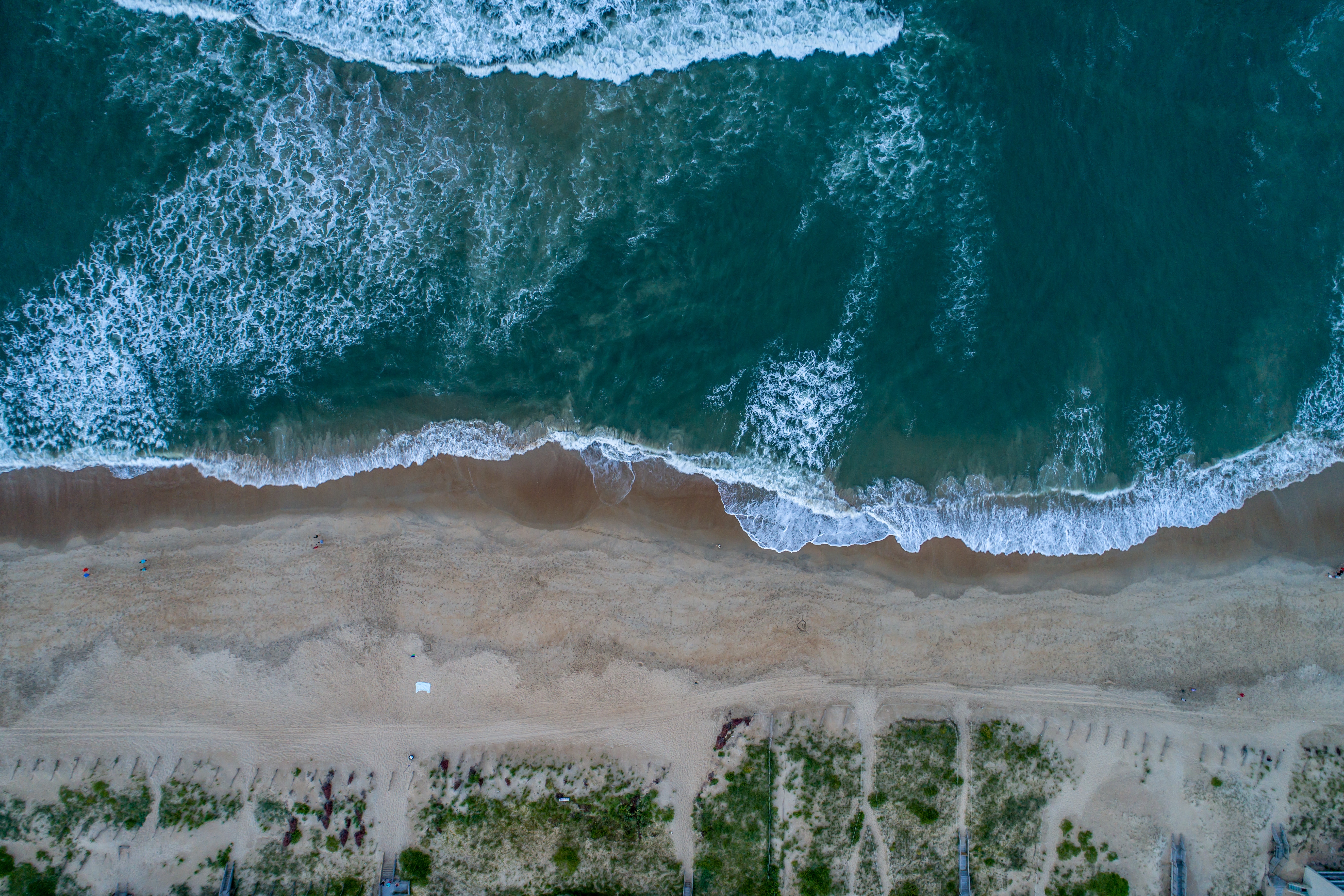 Aerial view of ocean waves crashing on a sandy beach HD Wallpaper