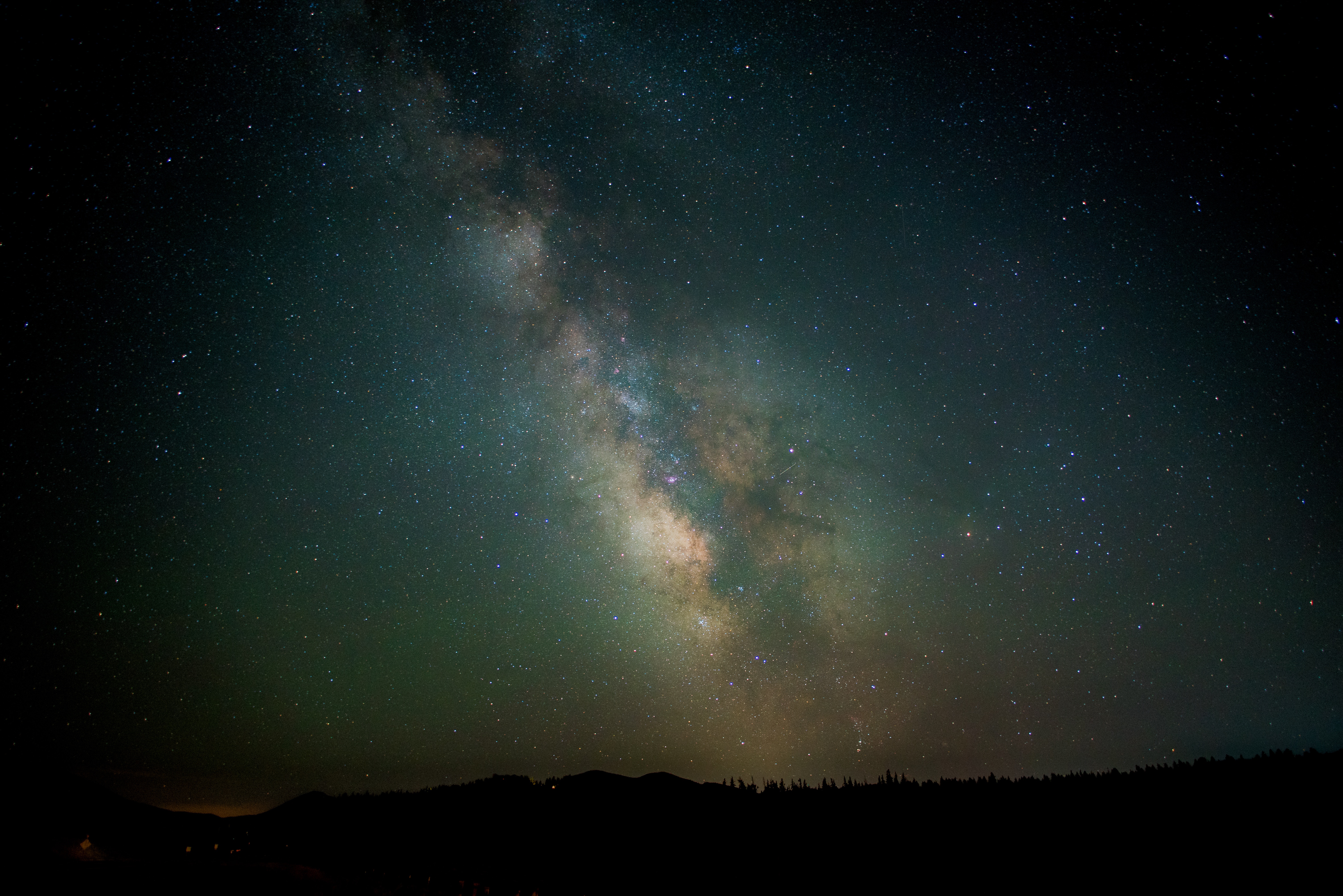 Milky Way galaxy over silhouetted trees and mountains HD Wallpaper