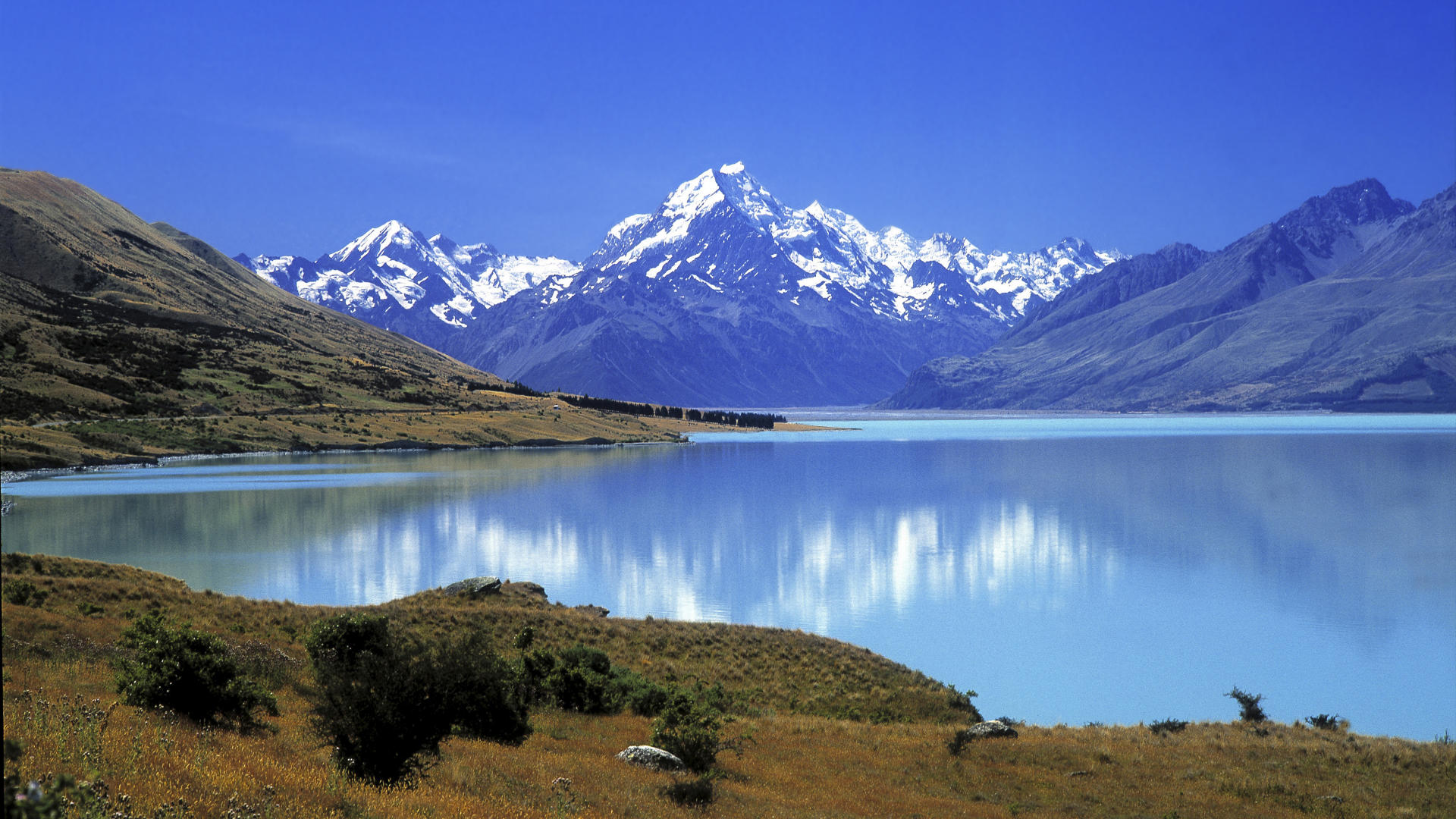 Snow-capped mountains reflected in a turquoise lake HD Wallpaper
