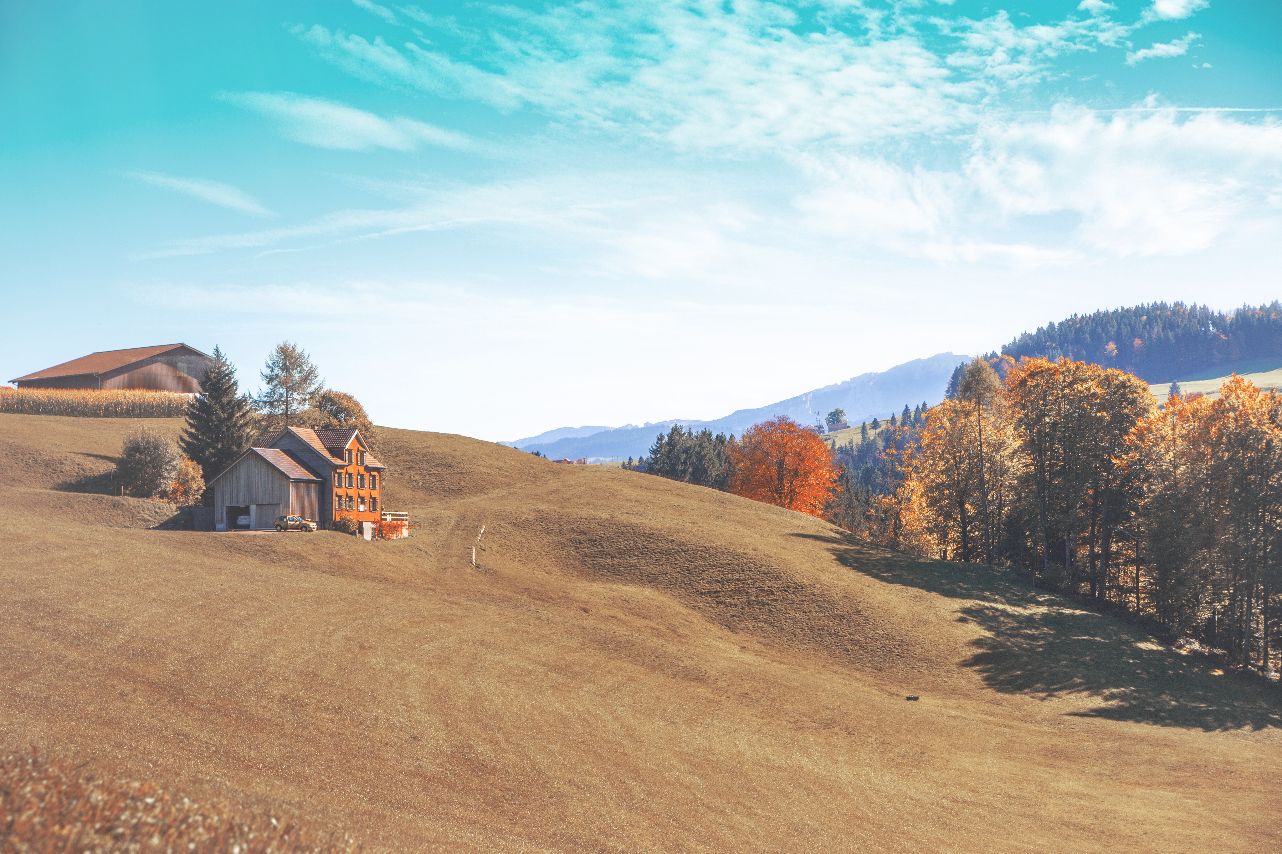 Farmhouse on a rolling hill with autumn trees and mountains HD Wallpaper