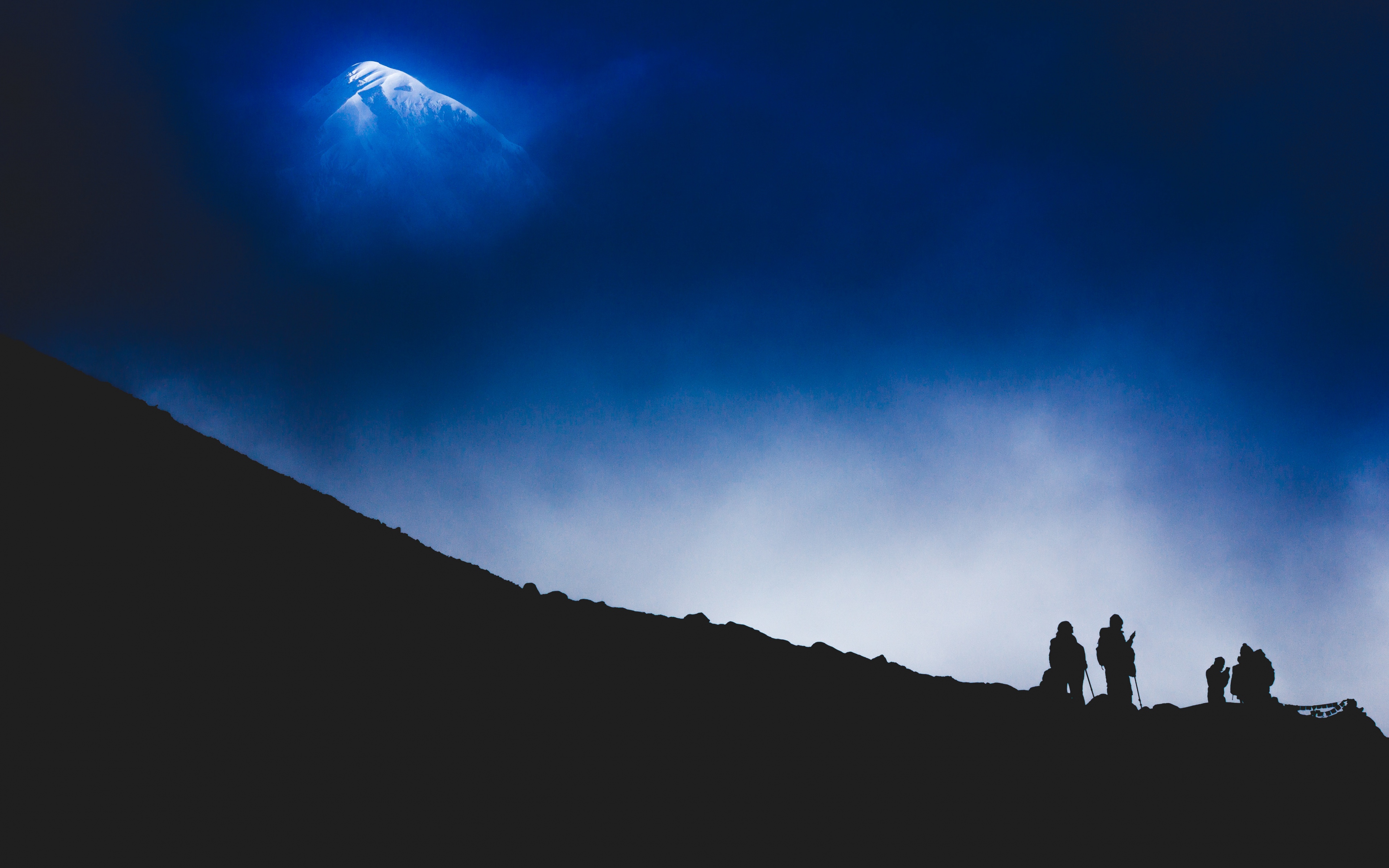 Silhouettes of hikers on a mountain slope with a snowy peak in the distance HD Wallpaper