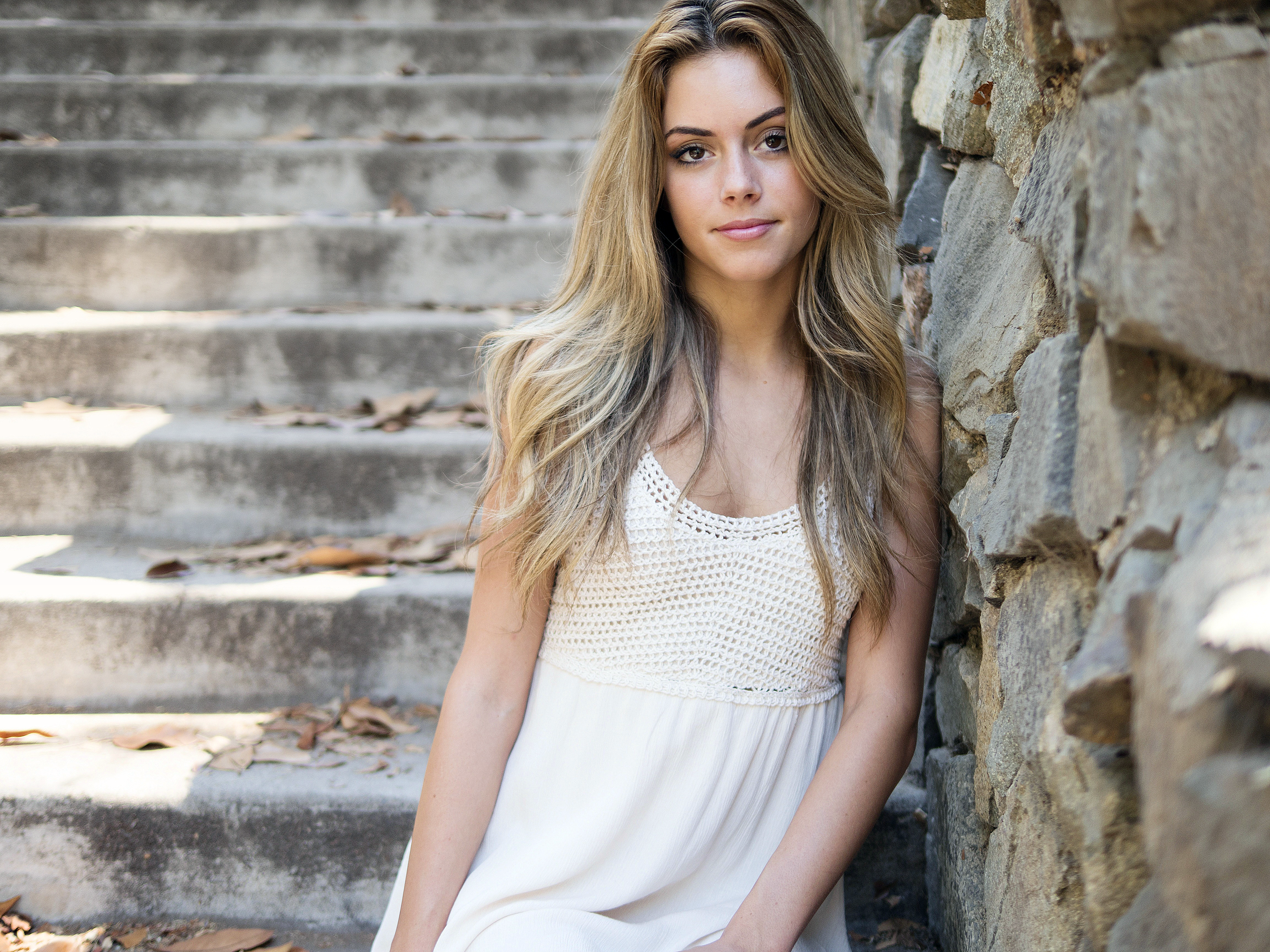 Young woman in white dress leaning against stone wall HD Wallpaper