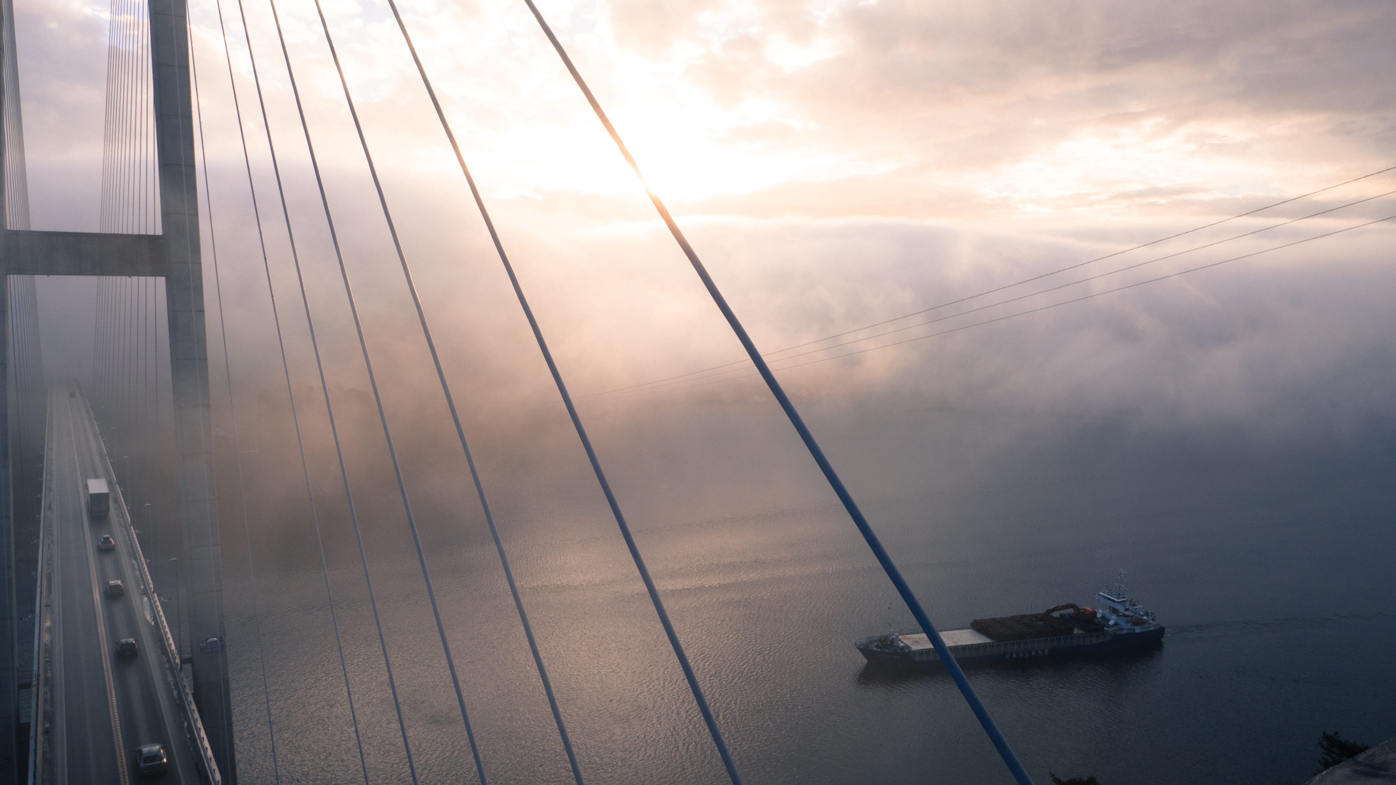 Cargo ship sailing under a foggy suspension bridge HD Wallpaper