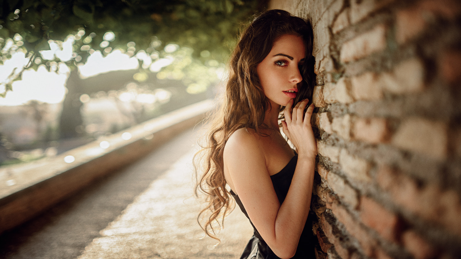 Woman with long wavy auburn hair leaning against a brick wall HD Wallpaper