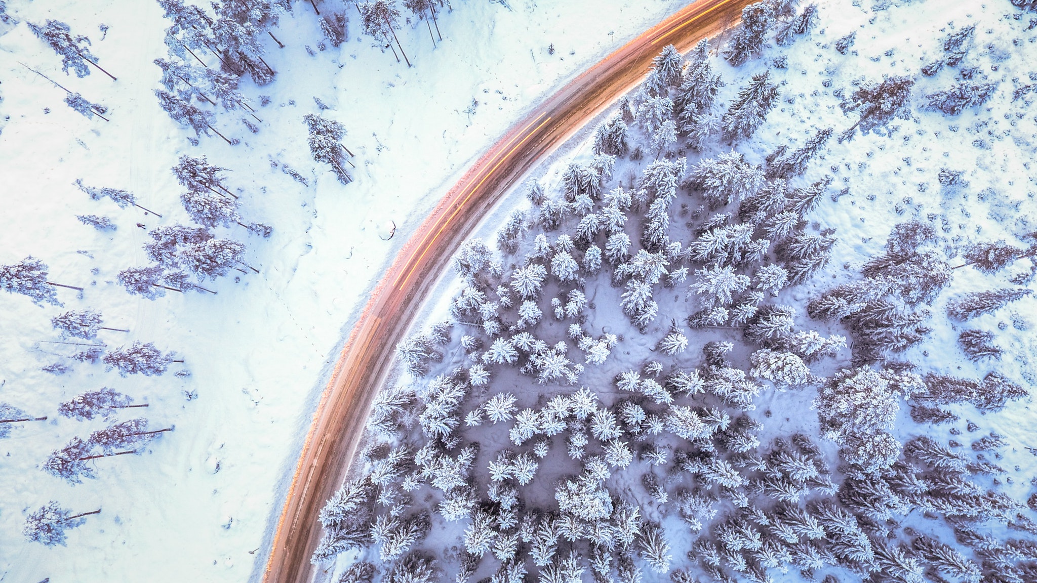 Aerial view of a snow-covered forest with a road HD Wallpaper