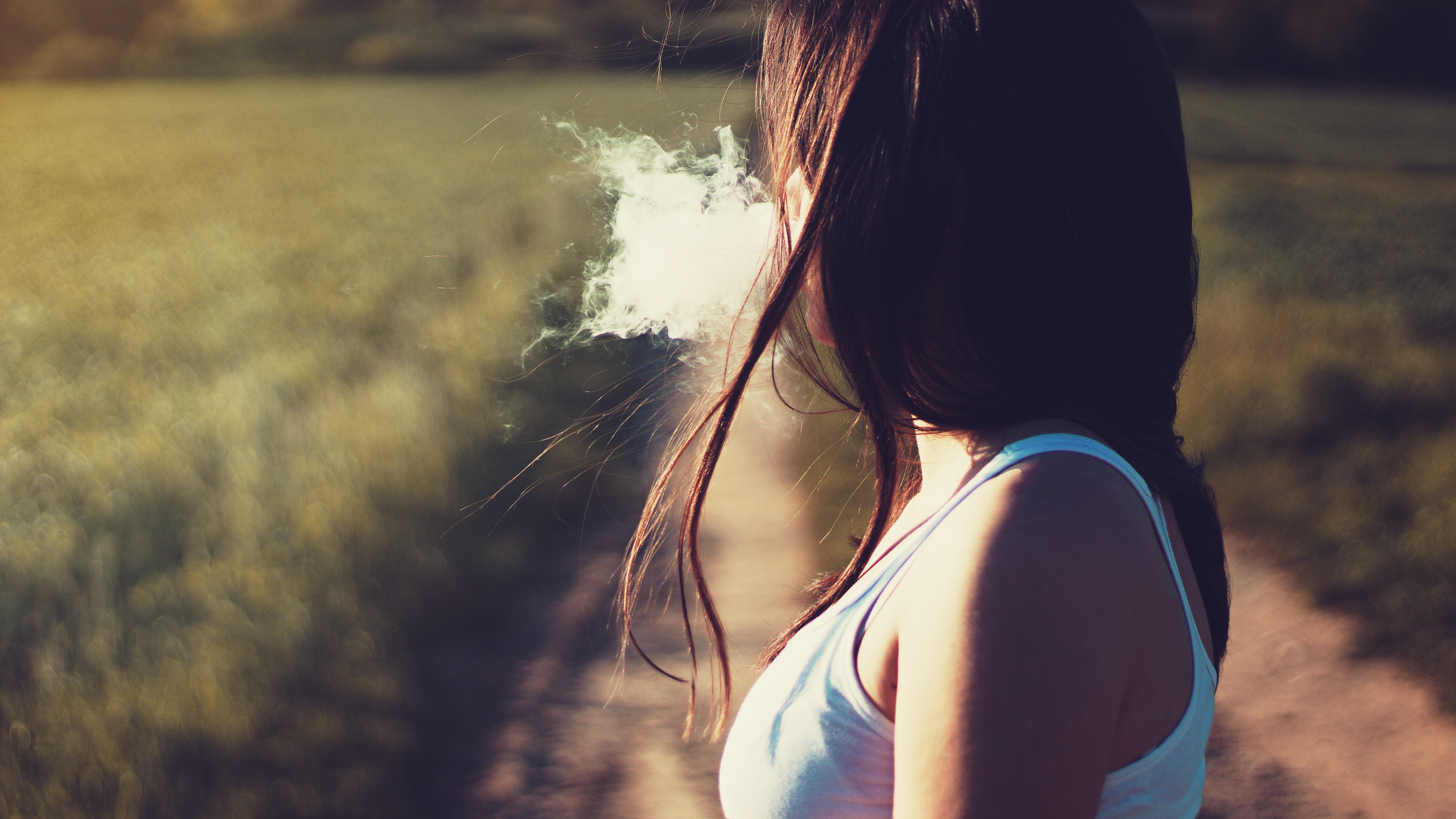 Woman exhaling smoke in a field HD Wallpaper
