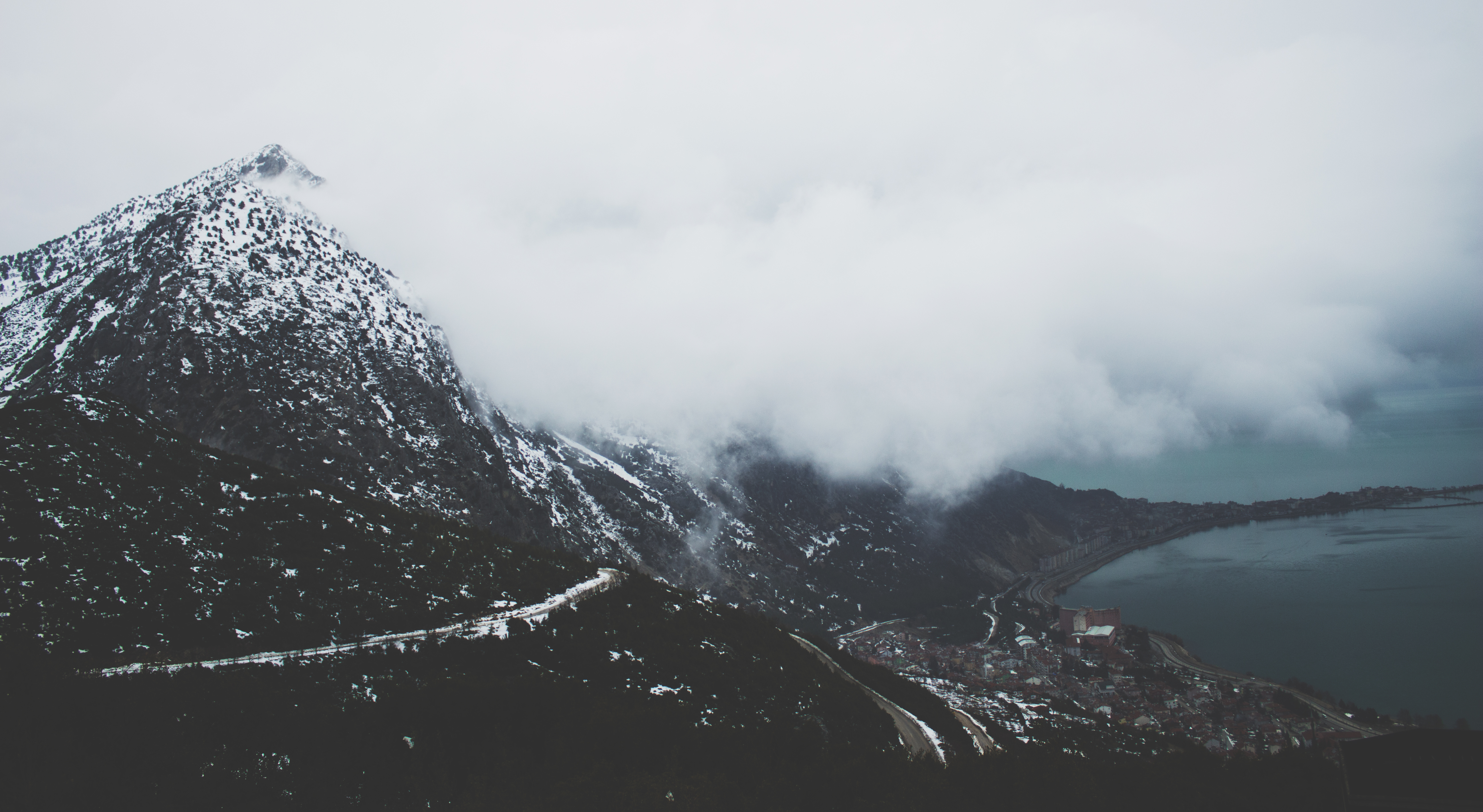 Snow-capped mountain overlooking a coastal town and sea HD Wallpaper