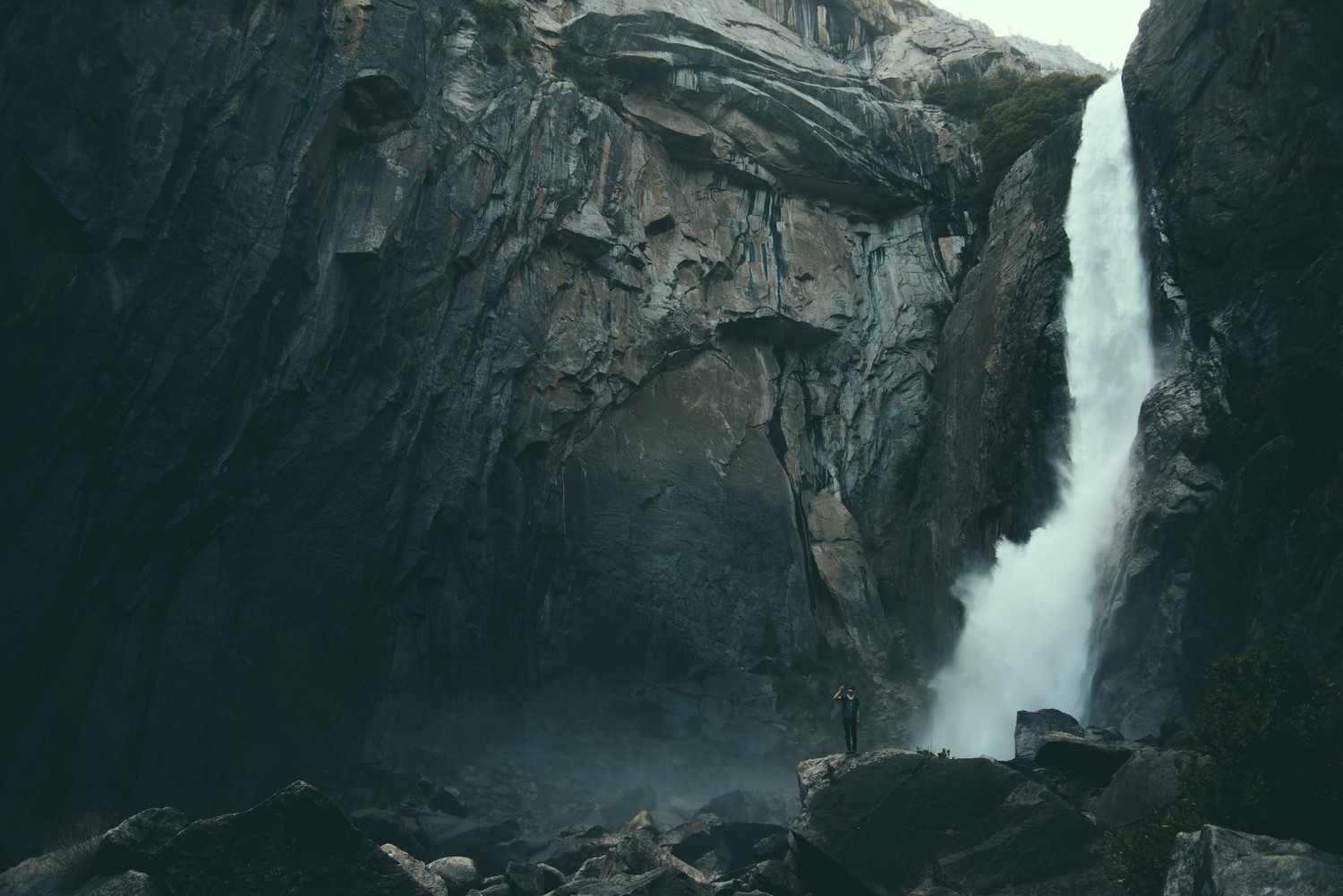 Man photographing a tall waterfall in a rocky canyon HD Wallpaper