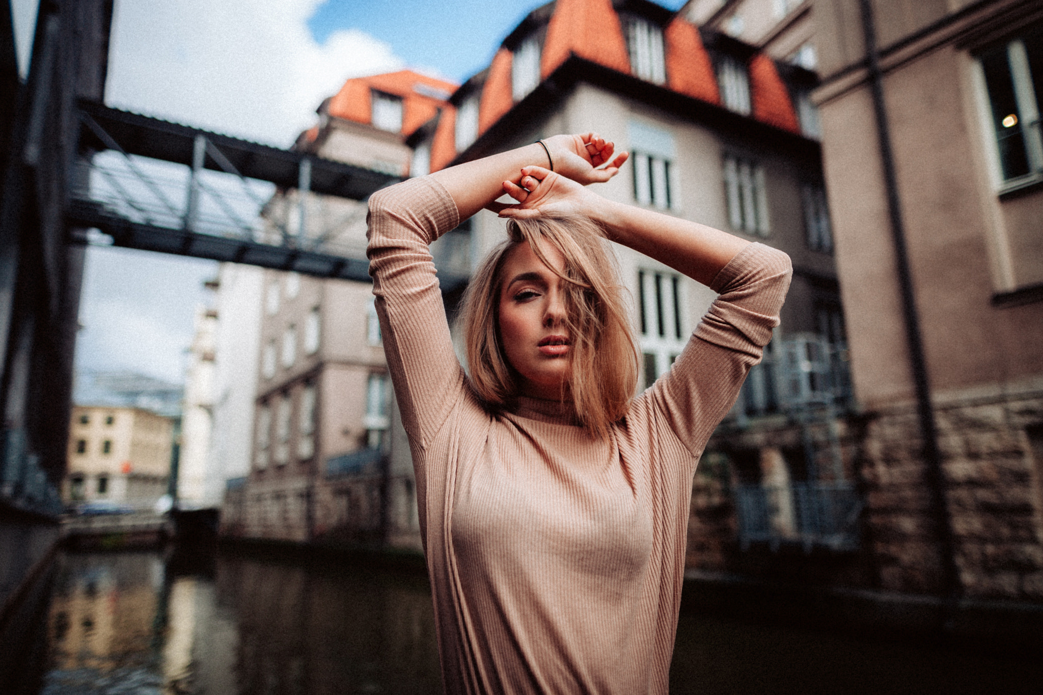 Woman with arms raised in front of buildings and canal HD Wallpaper
