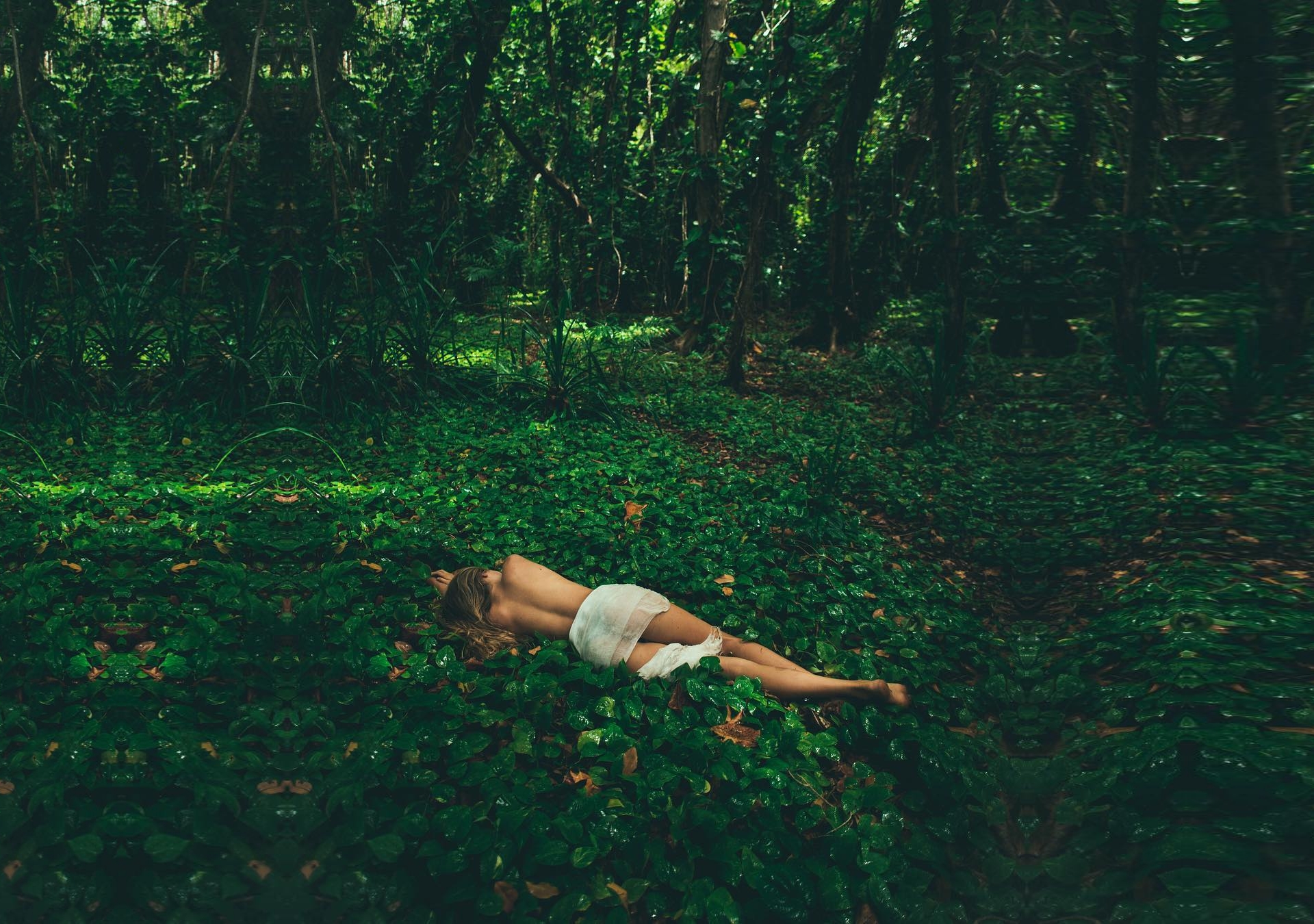 Woman lying in a green forest covered in leaves HD Wallpaper