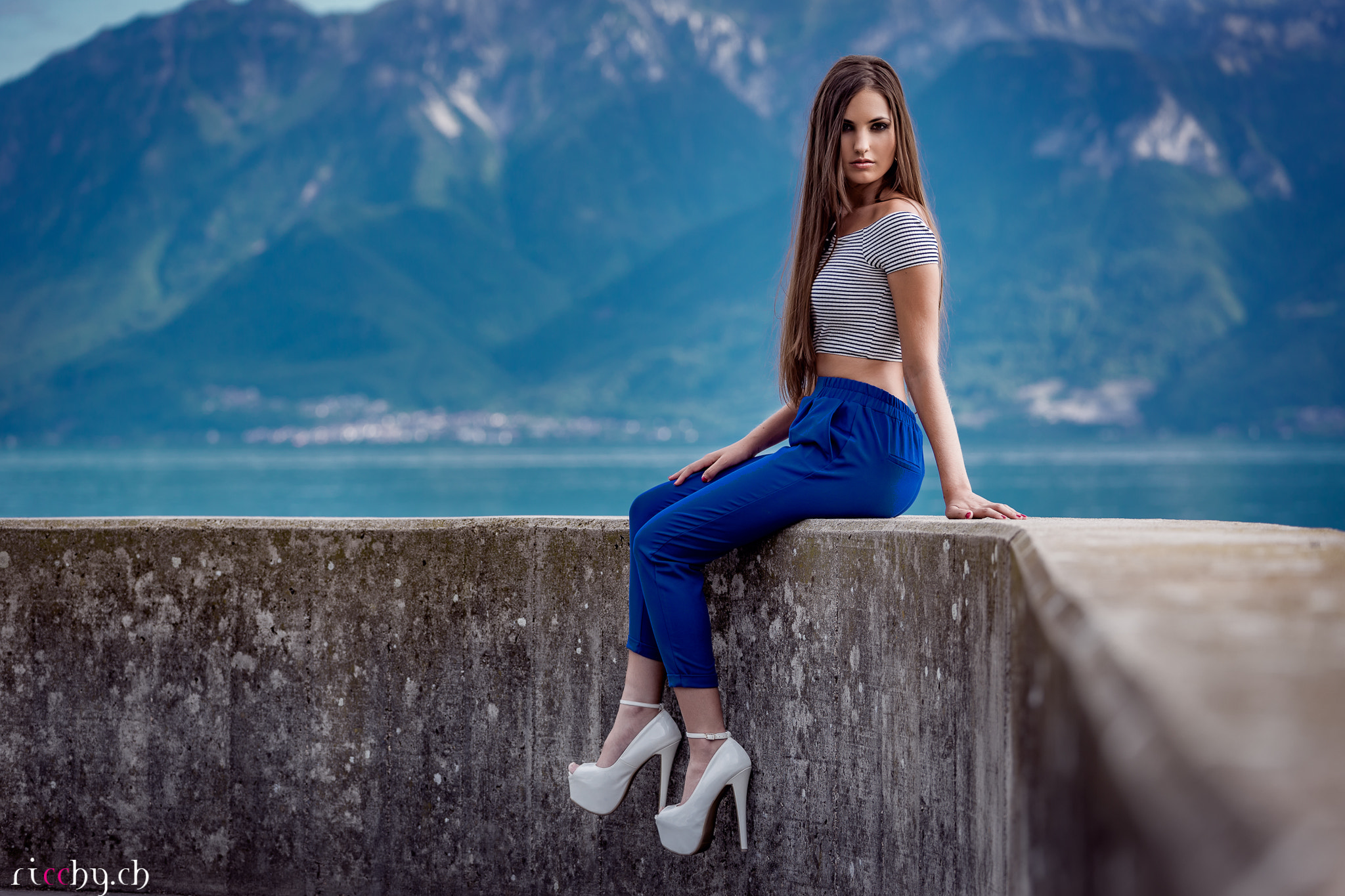 Woman in striped crop top and blue pants sitting by lake HD Wallpaper