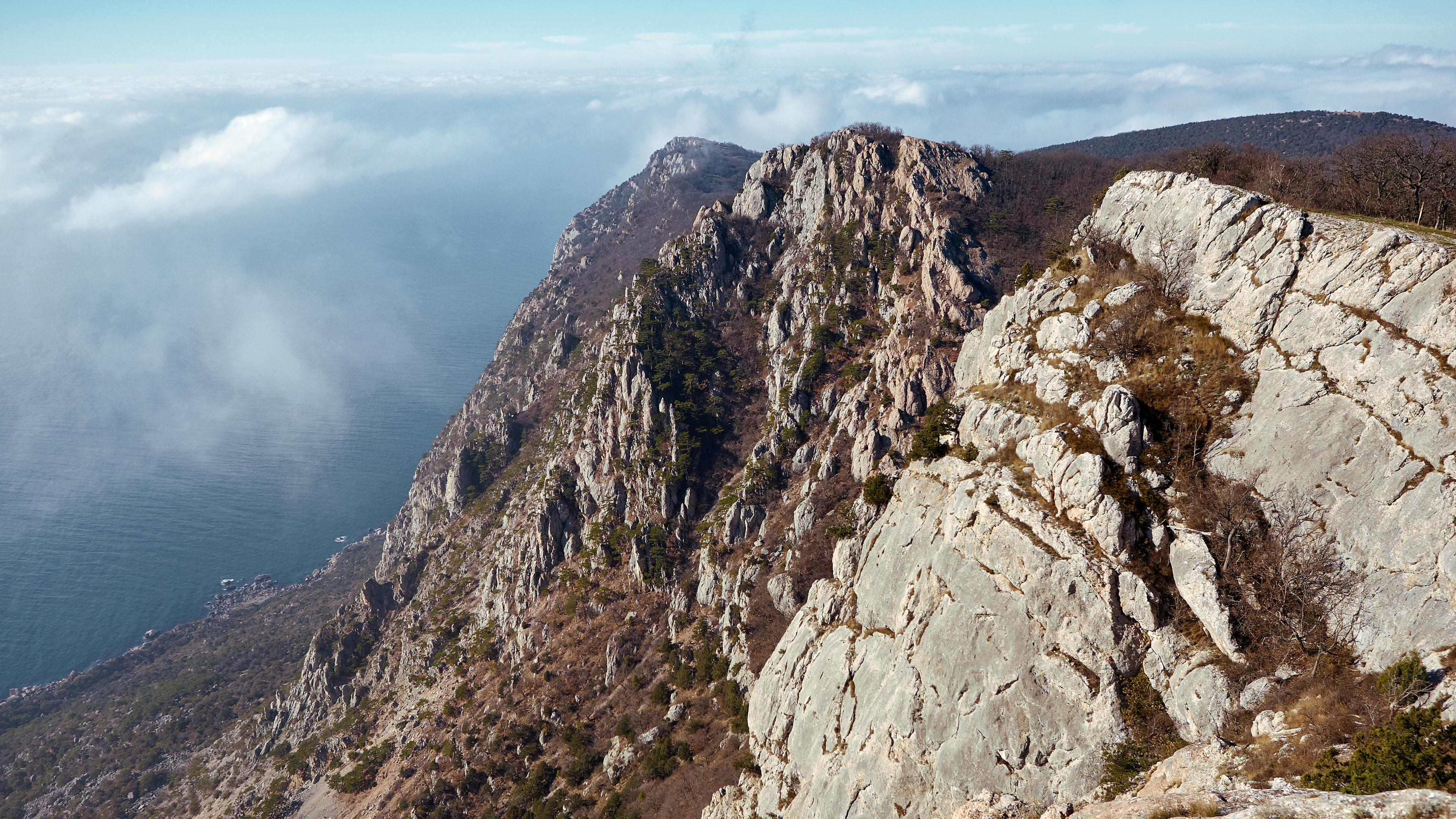 Rocky mountains overlooking the sea with clouds HD Wallpaper