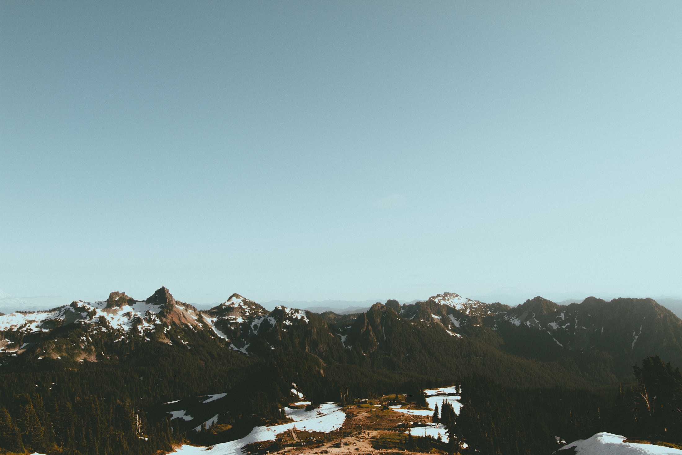 Snow-capped mountains with evergreen trees under a clear sky HD Wallpaper