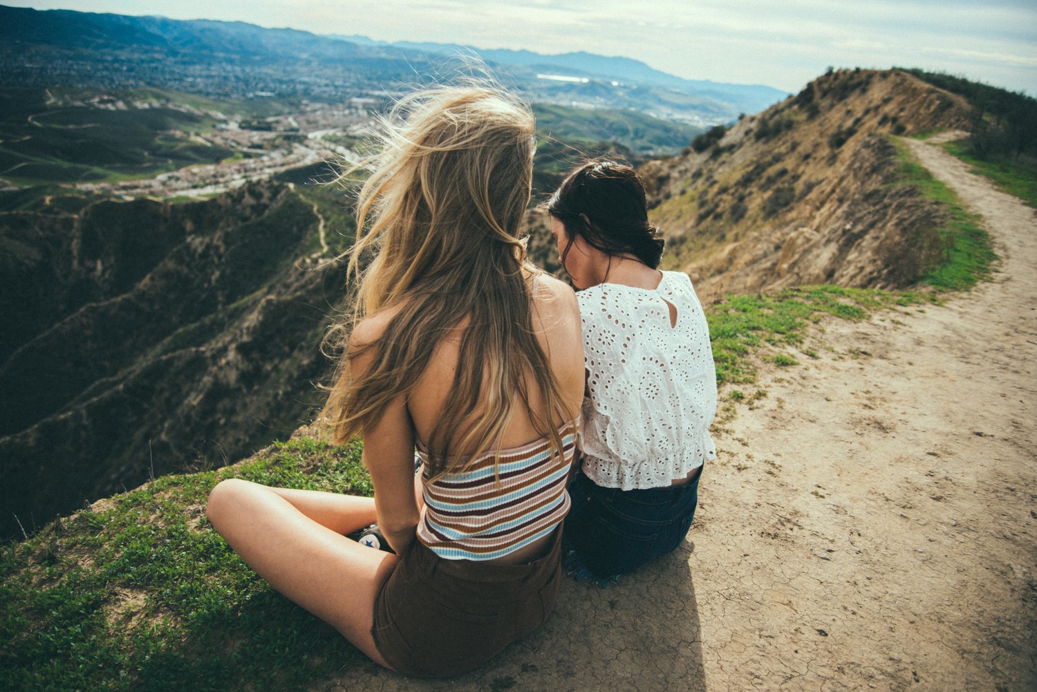 Two women sitting on a mountain overlooking a valley HD Wallpaper