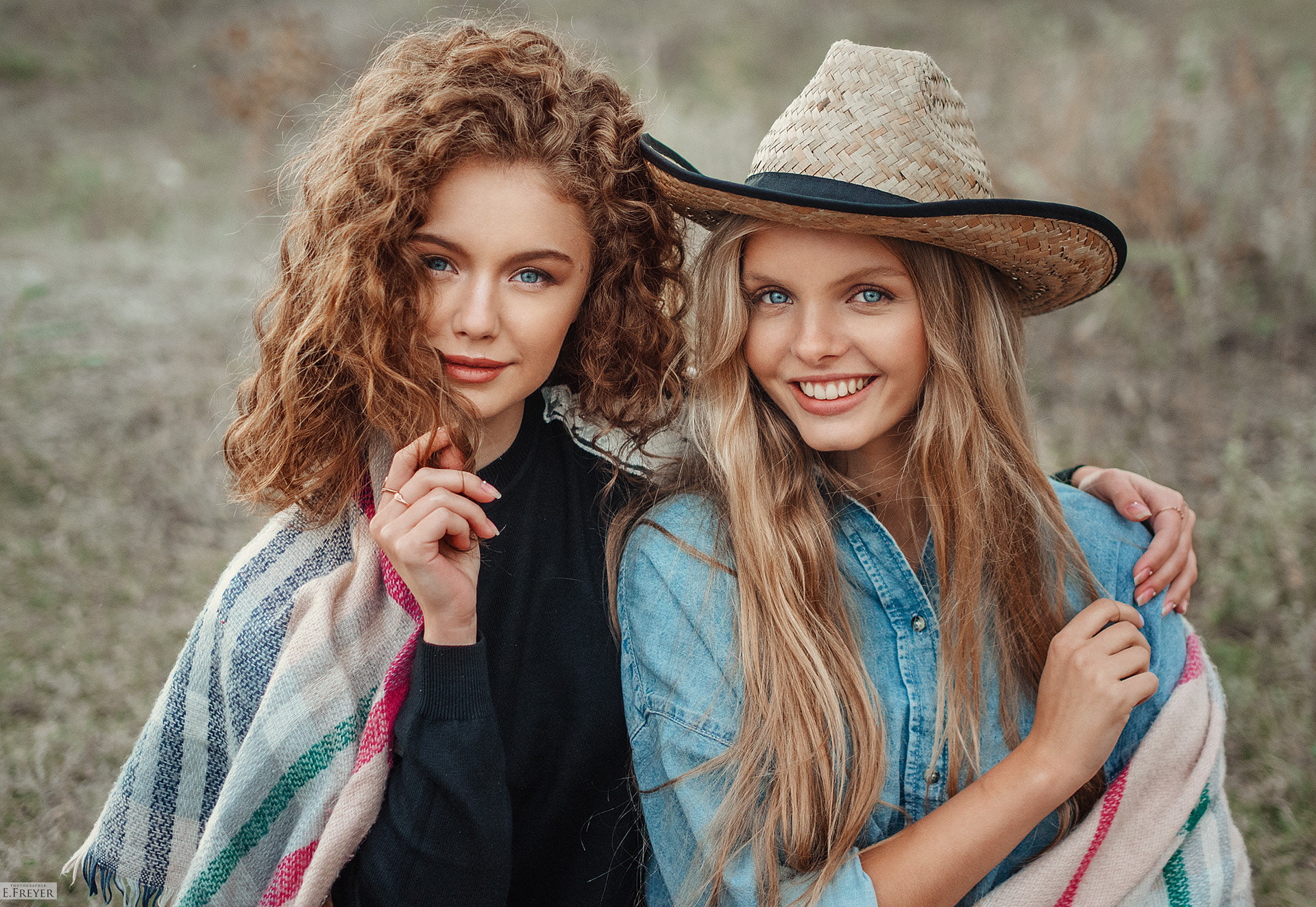 Two young women with curly and straight hair, one wearing a hat HD Wallpaper