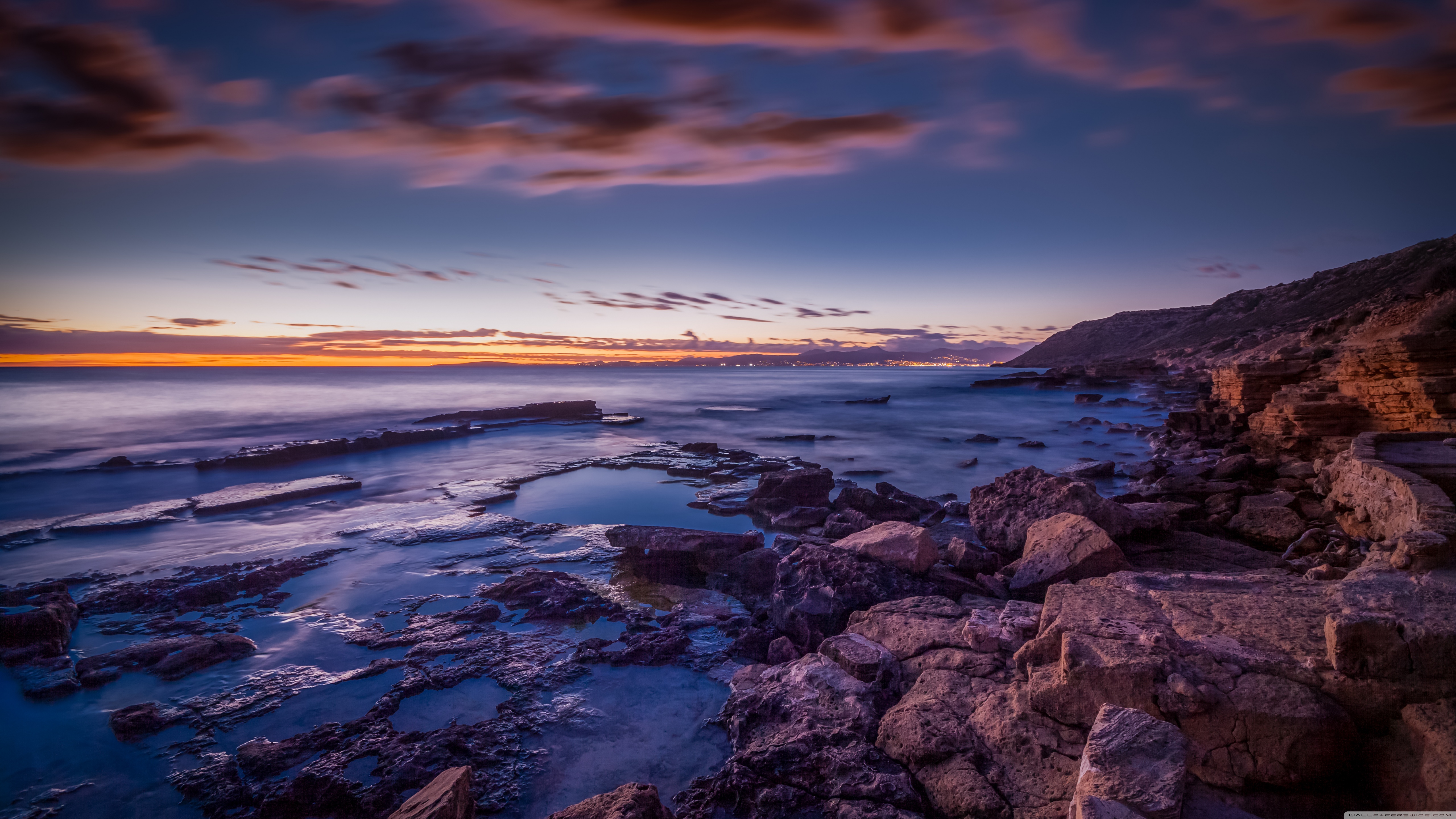 Rocky coastline at sunset with ocean waves HD Wallpaper