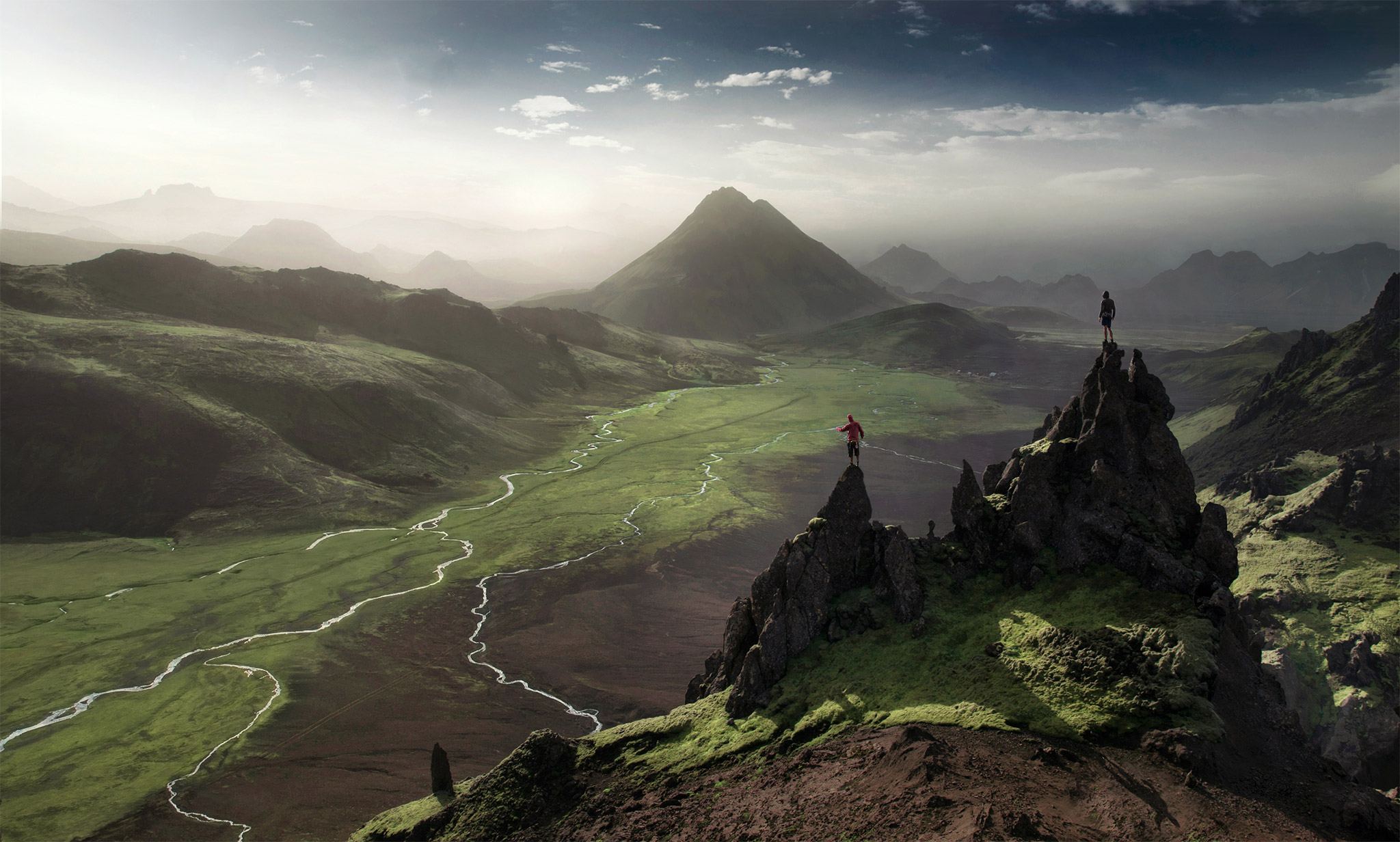 Two people on rocky peaks overlooking a valley HD Wallpaper