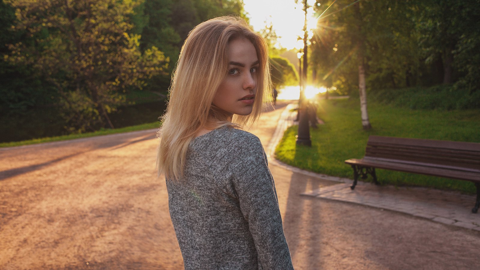 Woman with blonde hair looking over her shoulder in a park at sunset HD Wallpaper