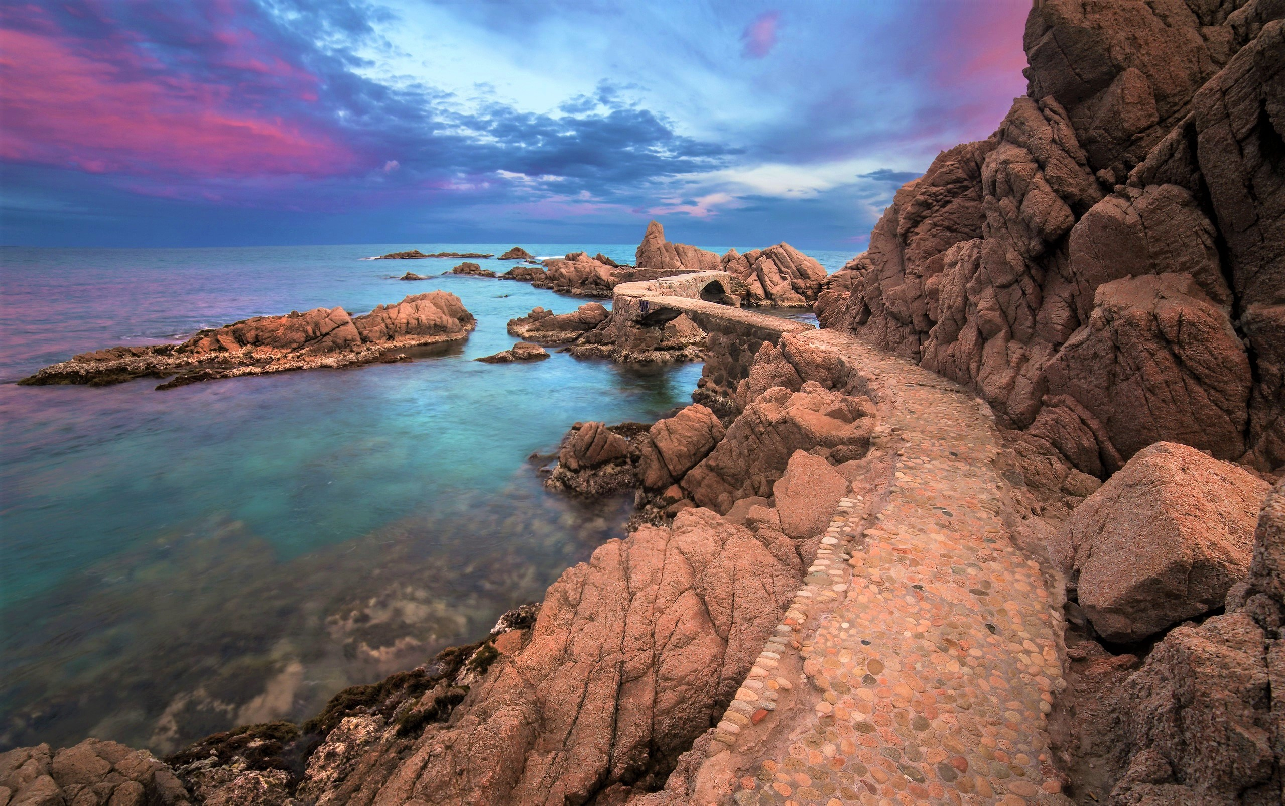 Rocky coast with stone path and bridge at sunset HD Wallpaper