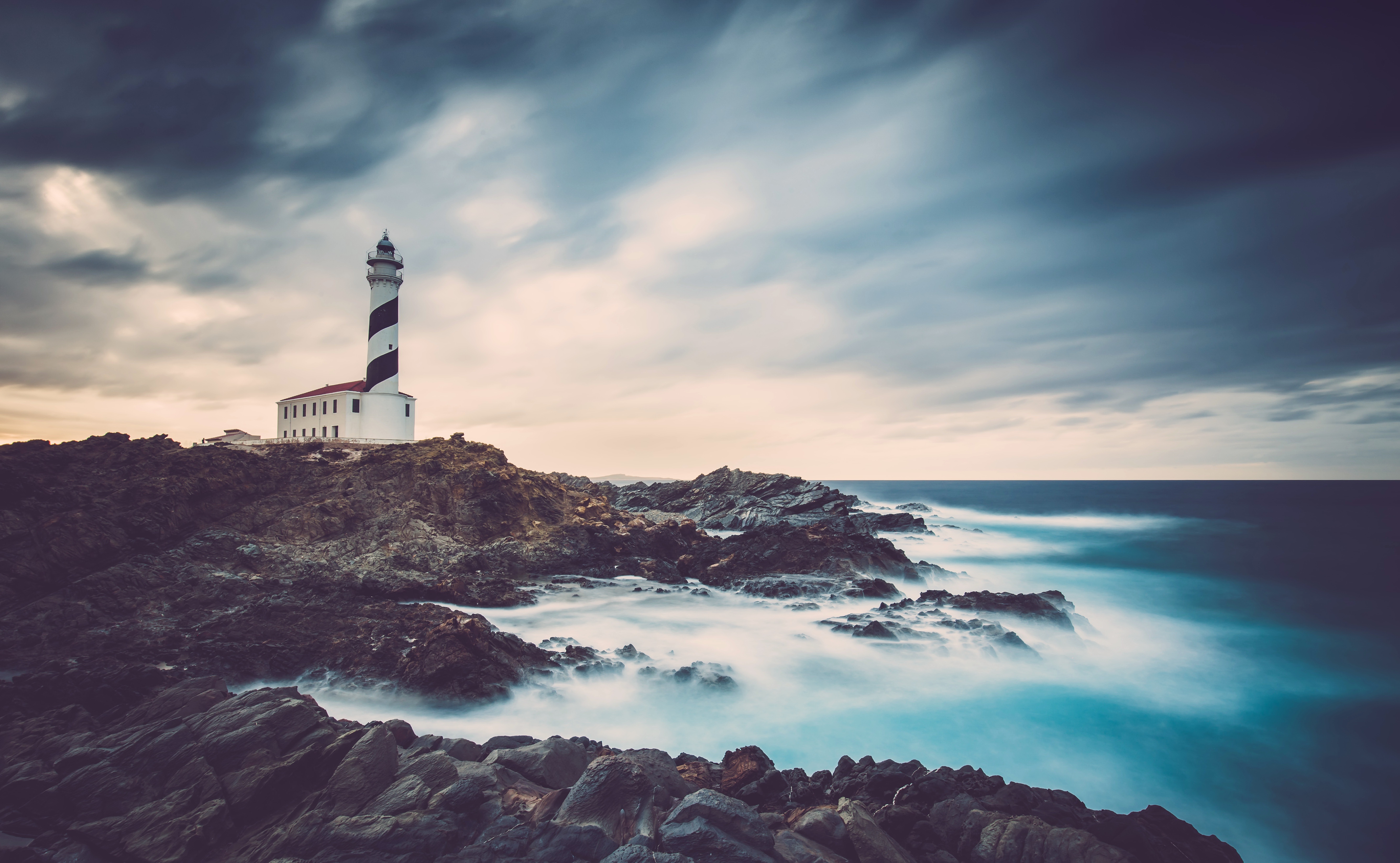 Lighthouse on rocky coast with stormy sea HD Wallpaper